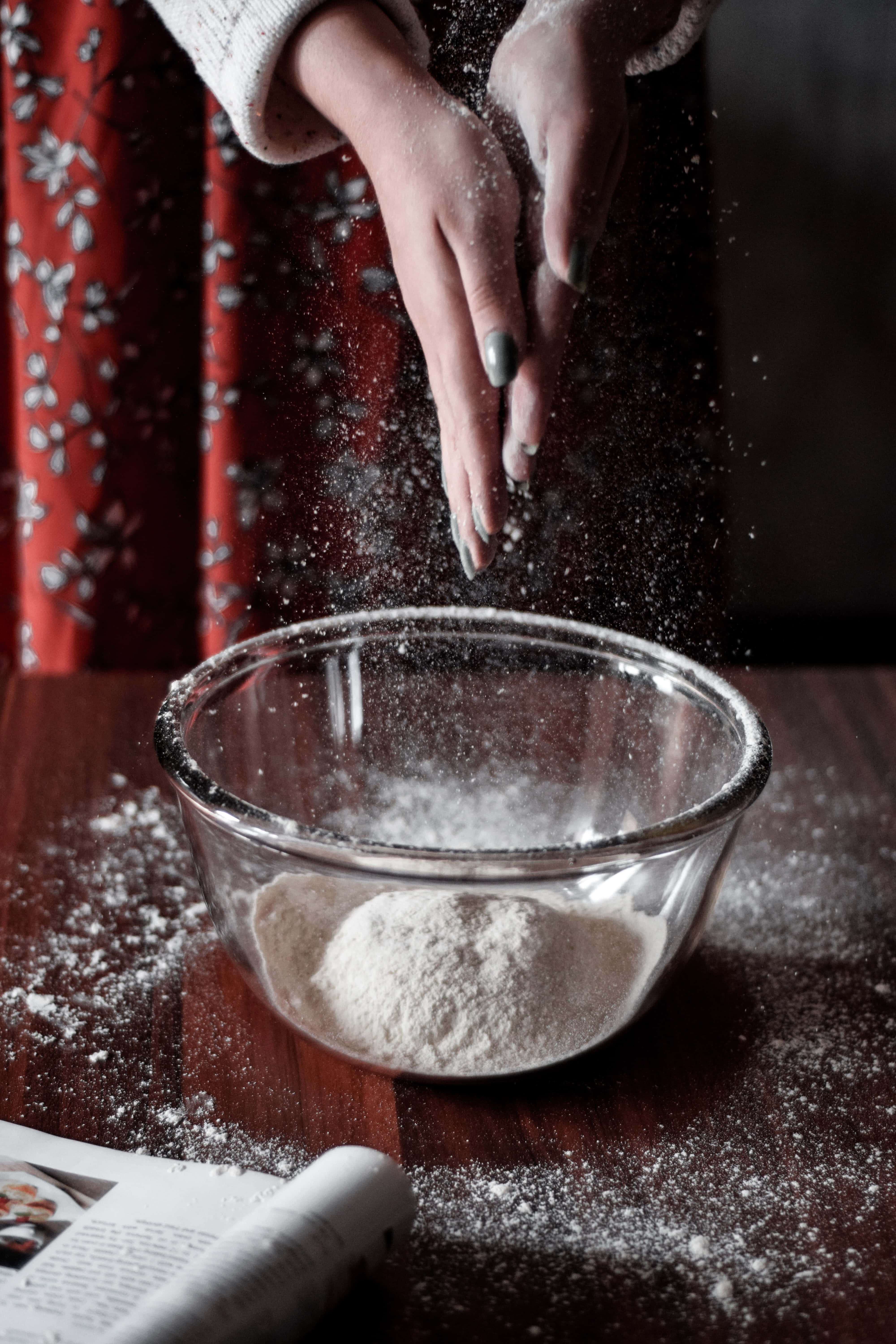 Baking 桌布 壁紙 — 一個人的雙手在木桌上的一個玻璃碗中撒麵粉，背景是紅色花卉窗簾。