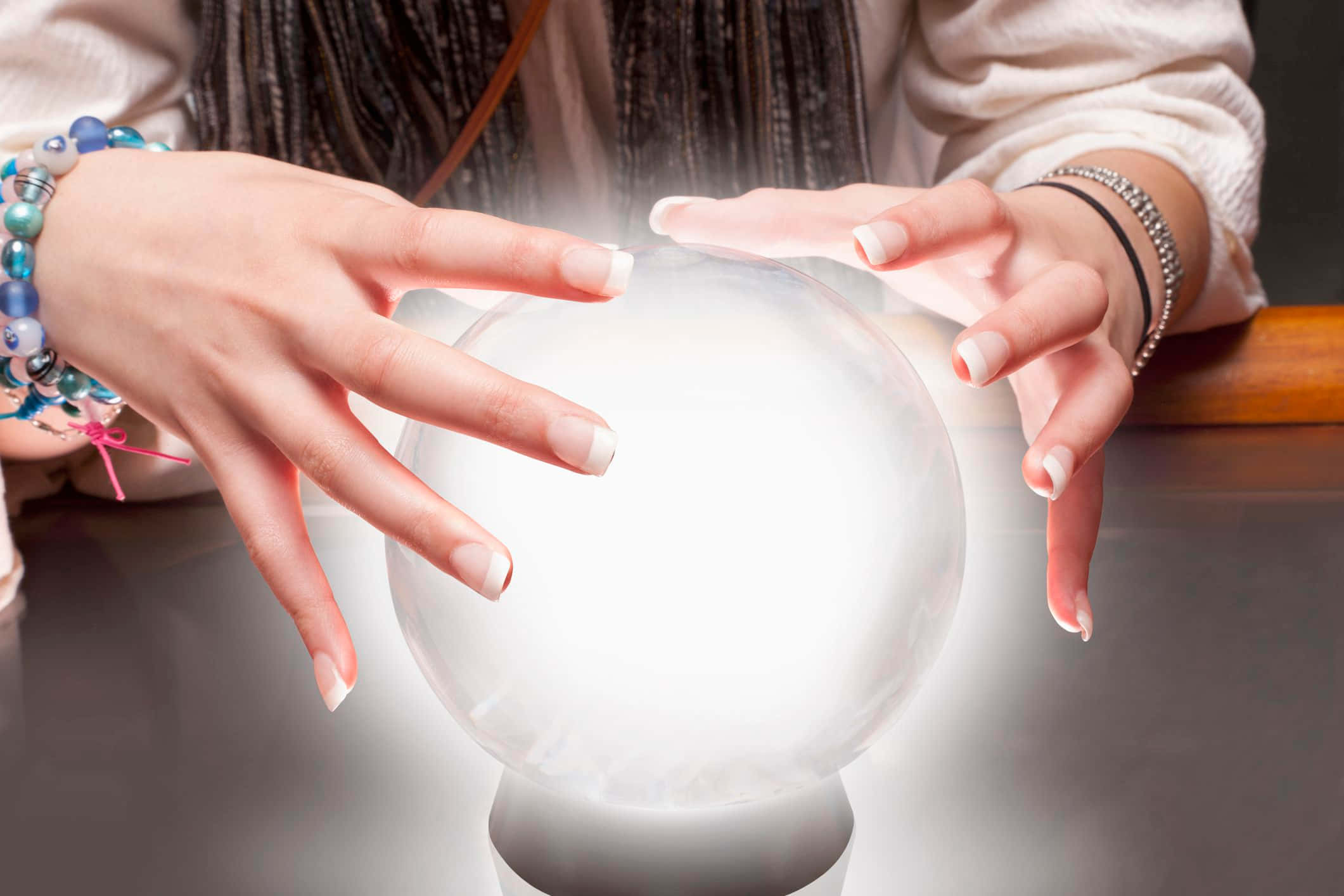 Crystal Ball 桌布 壁紙 — 一個人的雙手懸浮在一個發光的水晶球上方，散發出柔和的霧氣，置於暗色桌上。