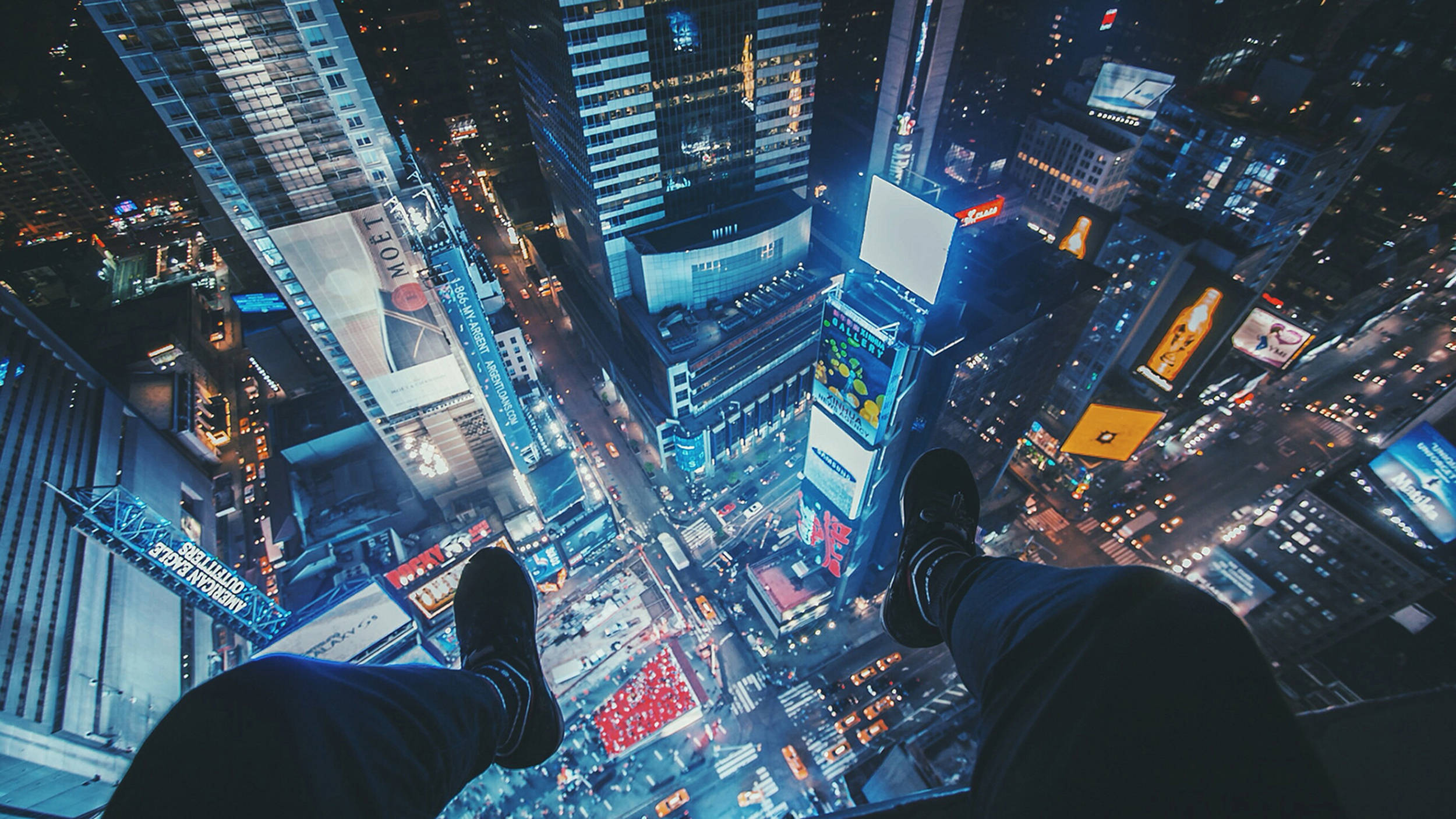 超炫動圖 桌布 壁紙 — 一個人的雙腳懸掛在璀璨的夜景城市上空，高聳的摩天大樓和發光的廣告牌盡收眼底。