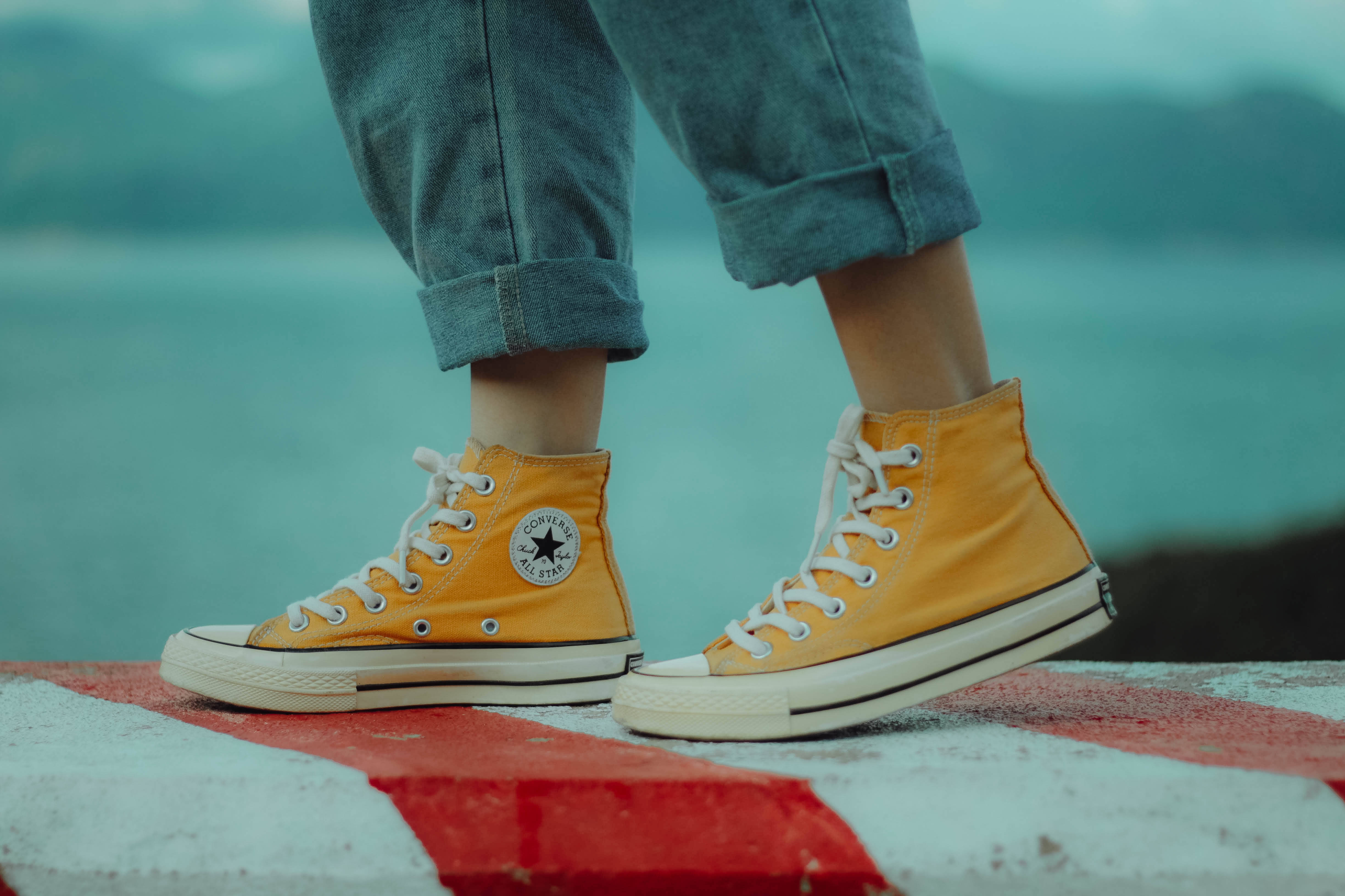 Converse 桌布 壁紙 — 一個人的黃色高筒運動鞋站在紅白條紋表面上，背景是模糊的藍綠色水面。