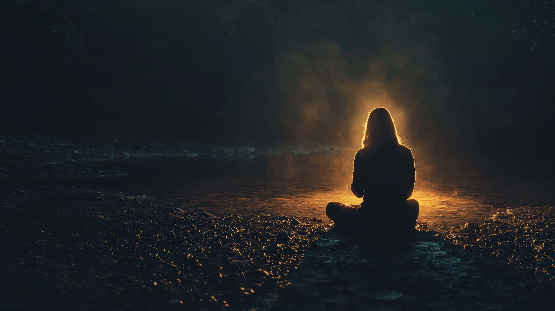 Silhouette of Person Meditating by a Fire 壁紙 — 一個人盤腿坐在河岸上，金色光芒穿過他們背後的薄霧。