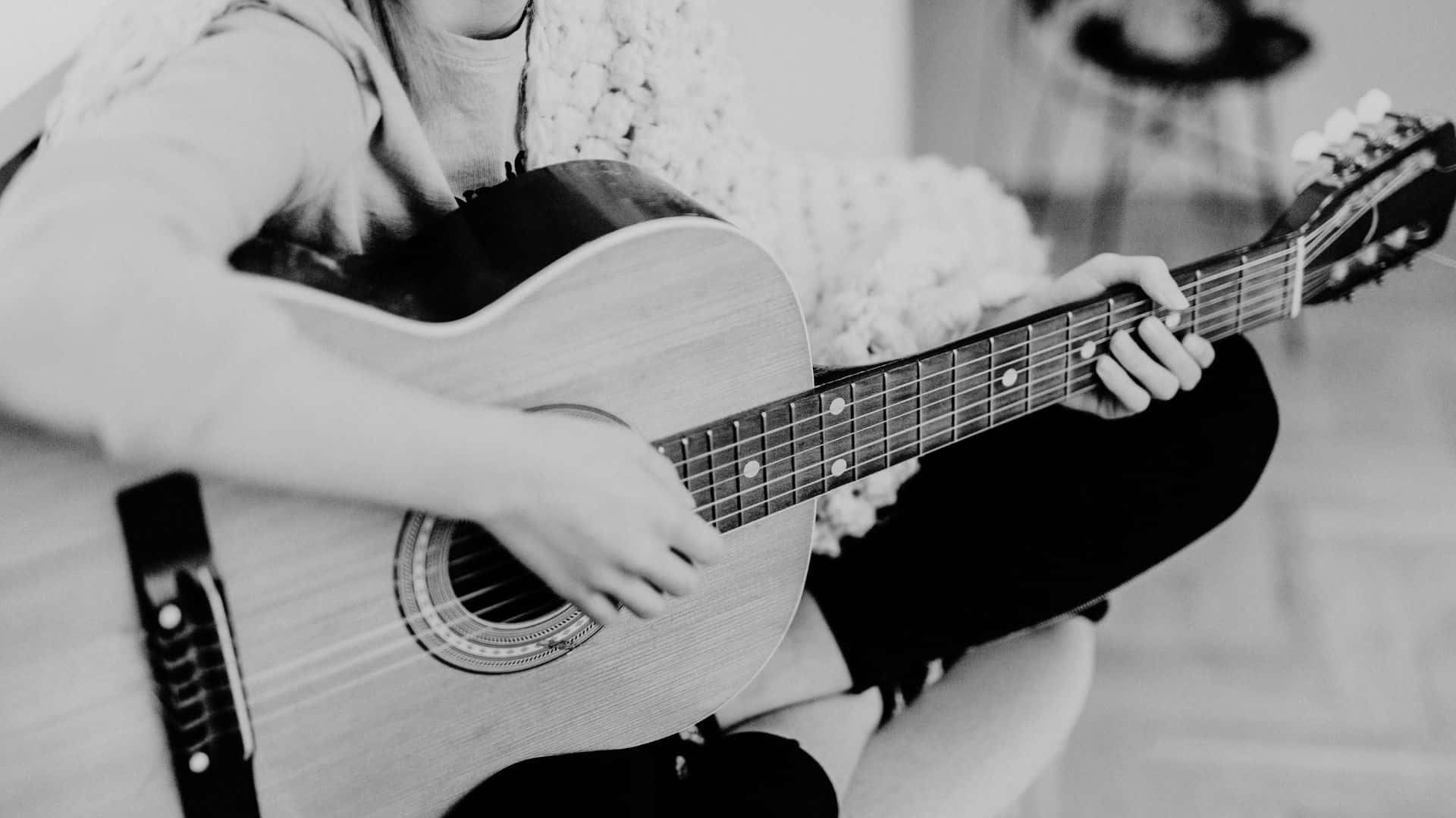 Black And White Guitar 桌布 壁紙 — 一個人盤腿坐著，在舒適的單色室內環境中彈奏木吉他。