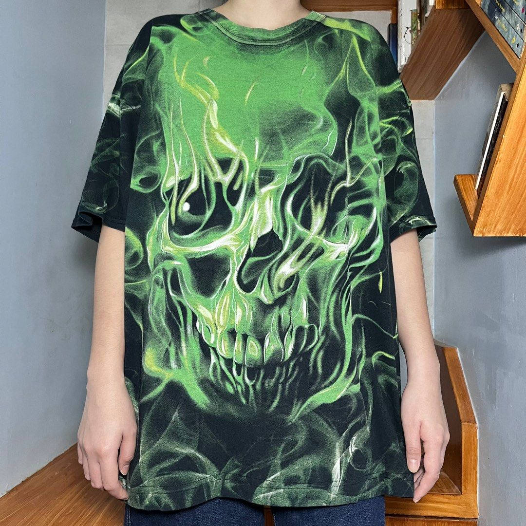 Green Fire Skull 桌布 壁紙 — 一個人穿著一件寬鬆的黑色T恤，上面有鮮豔的綠色骷髏圖案，看起來像發光的火焰。