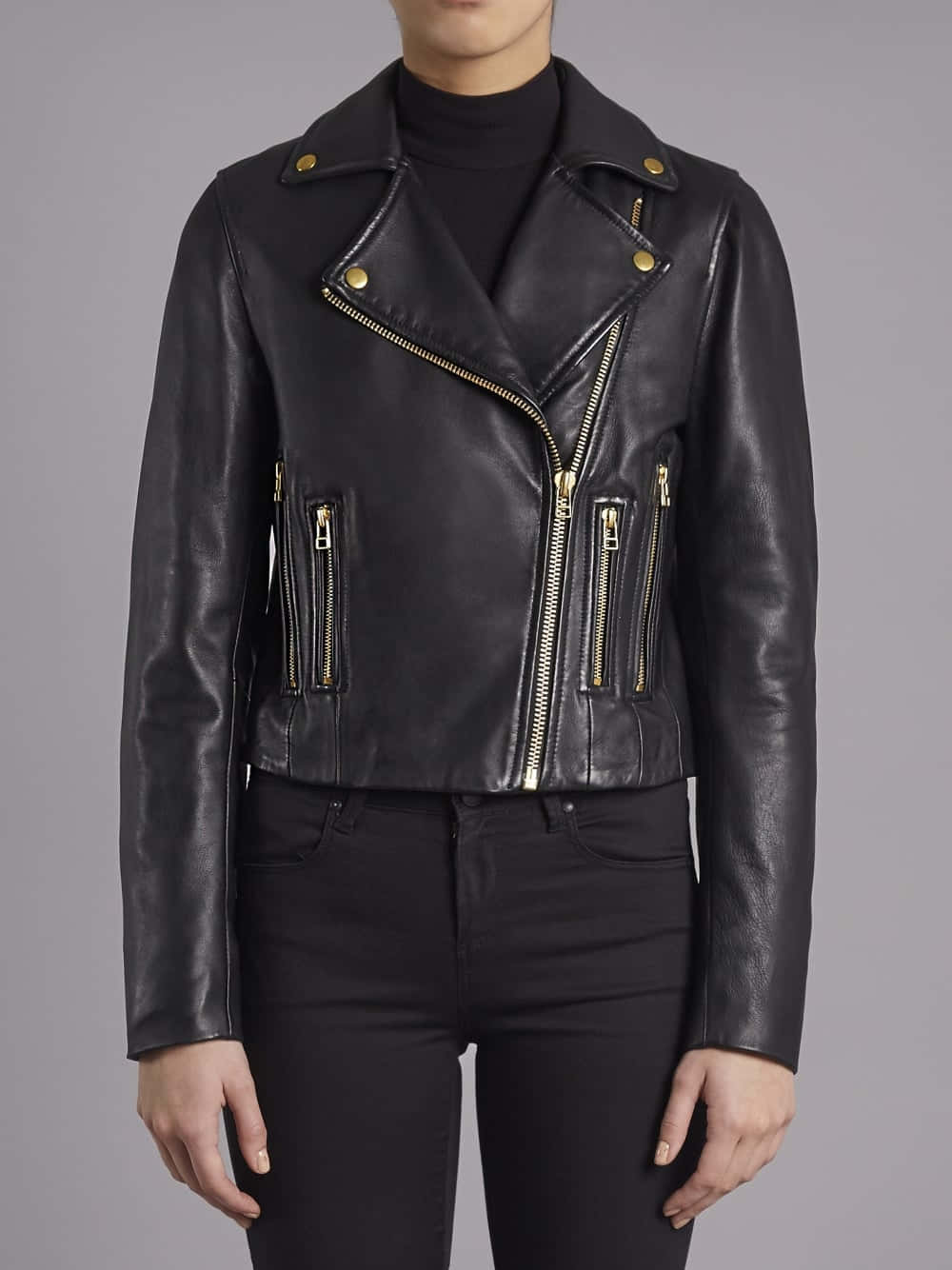 Black Leather 桌布 壁紙 — 一個人穿著一件時尚的黑色皮革機車外套，配有金色拉鍊，內搭黑色高領毛衣和牛仔褲，背景為中性灰色。