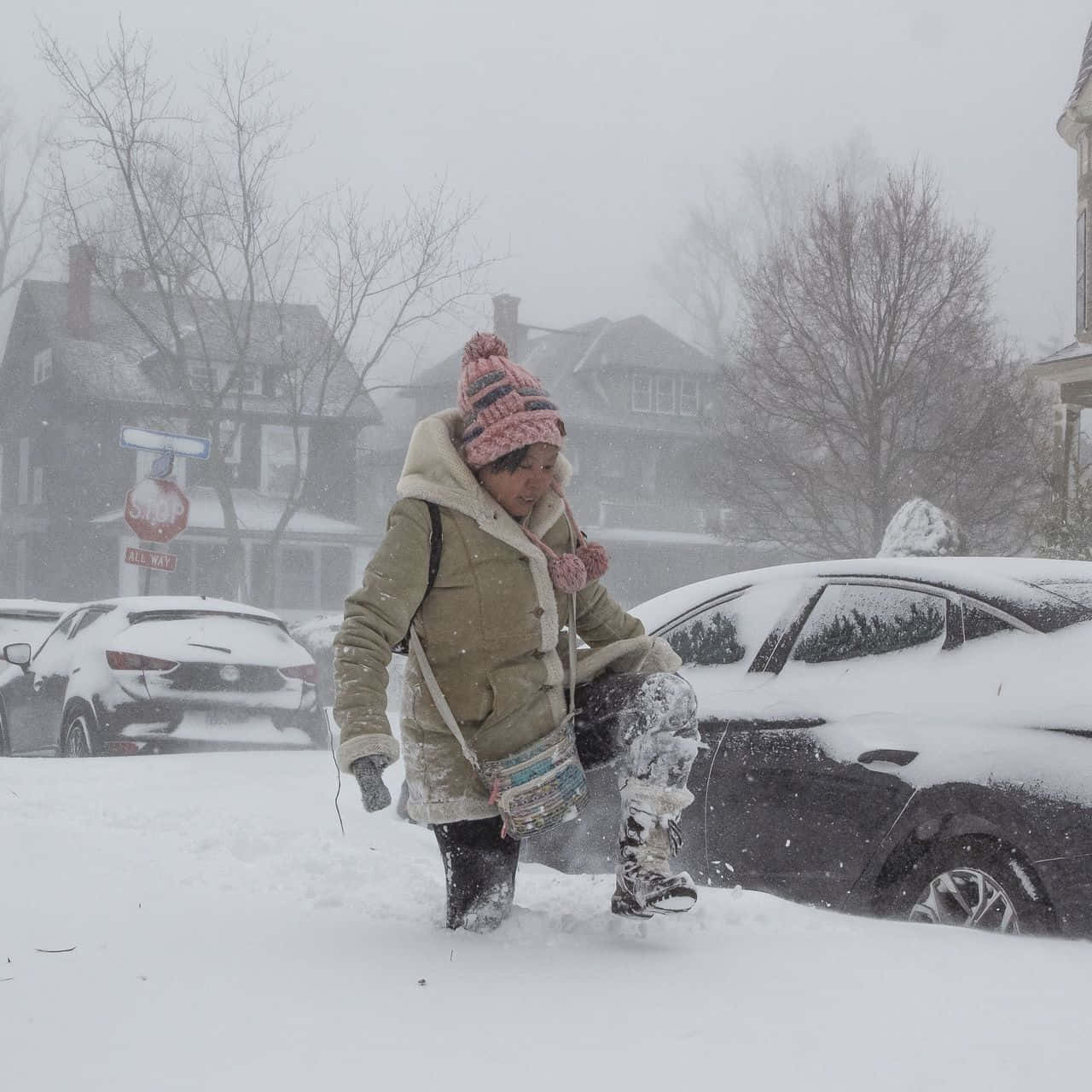 Winter 桌布 壁紙 — 一個人穿著冬季外套和針織帽，在暴風雪期間走過住宅區深雪中，旁邊是積雪的汽車。
