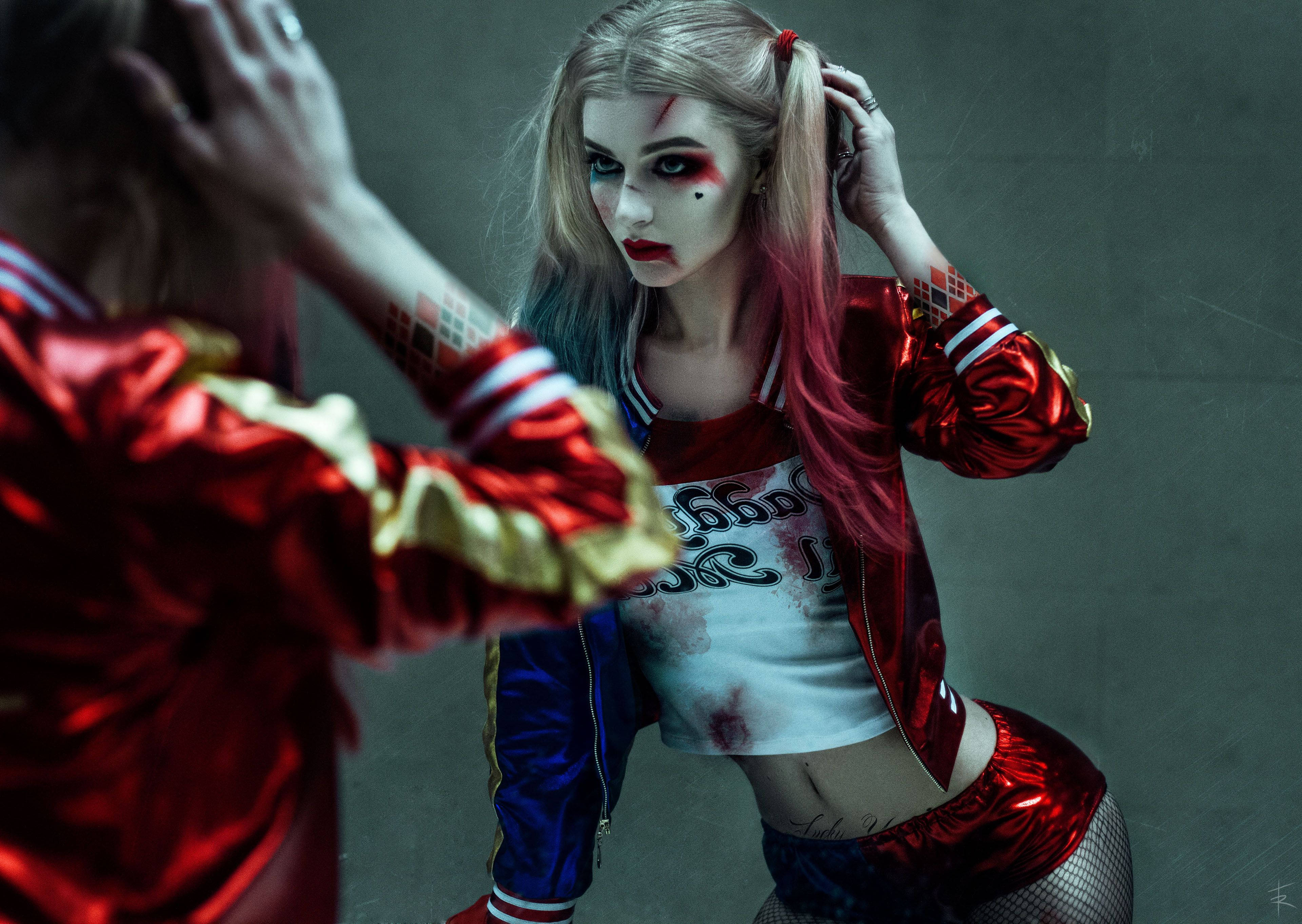 Harley 桌布 壁紙 — 一個人穿著哈莉·奎茵服裝，紅藍配色服裝和化妝污跡，在灰色牆前擺姿勢。