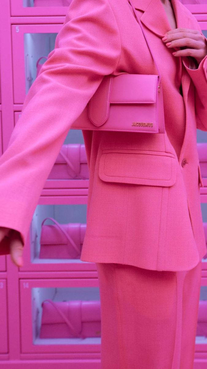 Pink Phone 桌布 壁紙 — 一個人穿著大膽的粉紅色西裝和相配的手袋，自信地站在充滿活力的粉紅色置物櫃牆前。