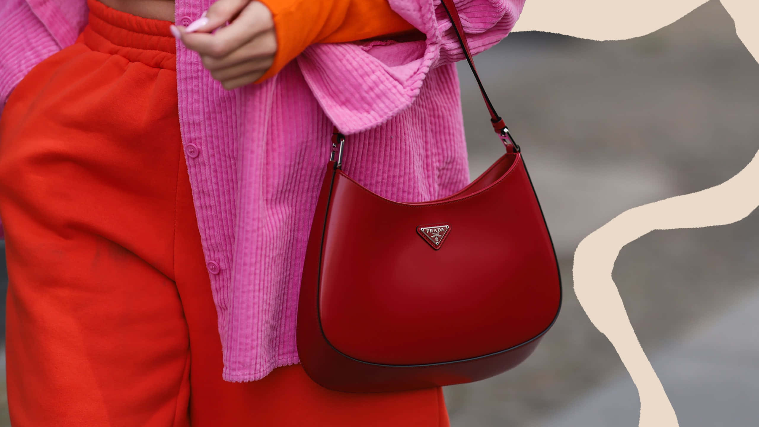 Red Handbag 桌布 壁紙 — 一個人穿著大膽的紅色和粉紅色燈芯絨服裝，在時尚的米色和灰色背景前拿著一個光澤的紅色Prada手提包。