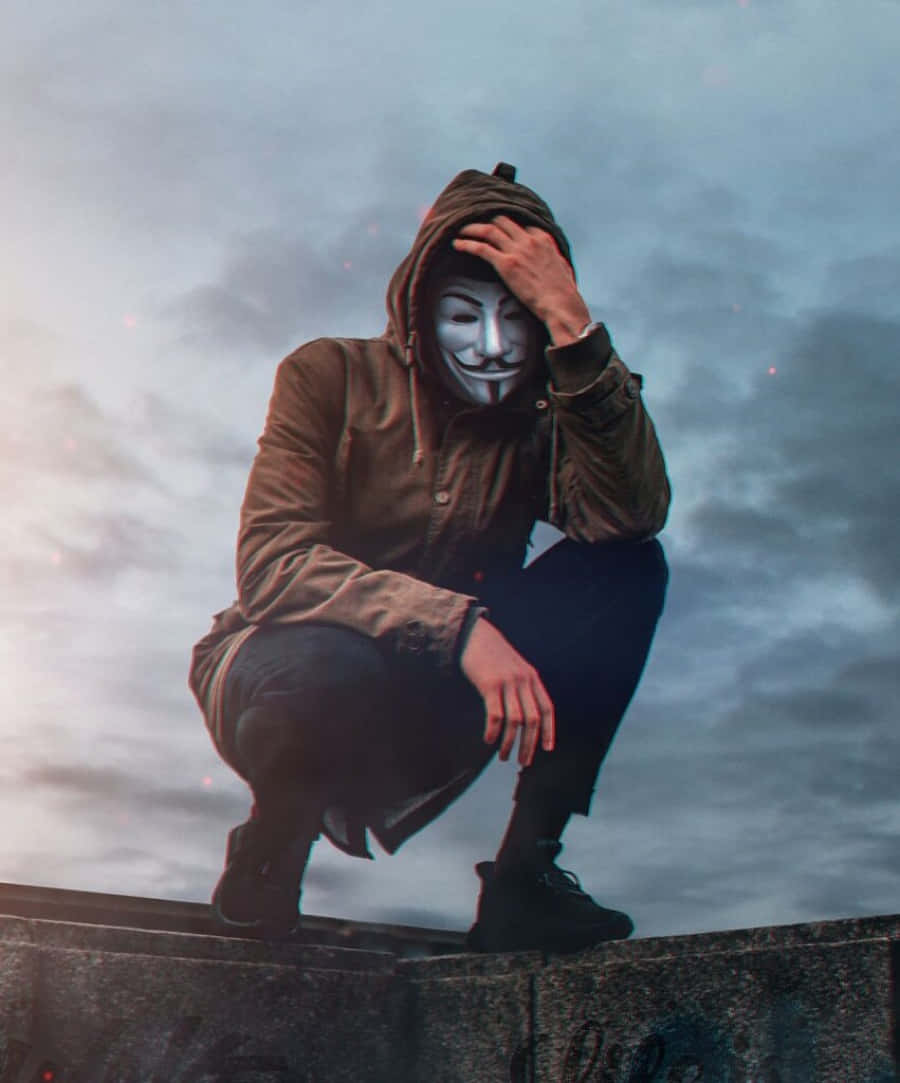 profile pic 桌布 壁紙 — 一個人穿著棕色連帽衫和白色蓋伊·福克斯面具，蹲在混凝土邊緣上，背景是陰天。