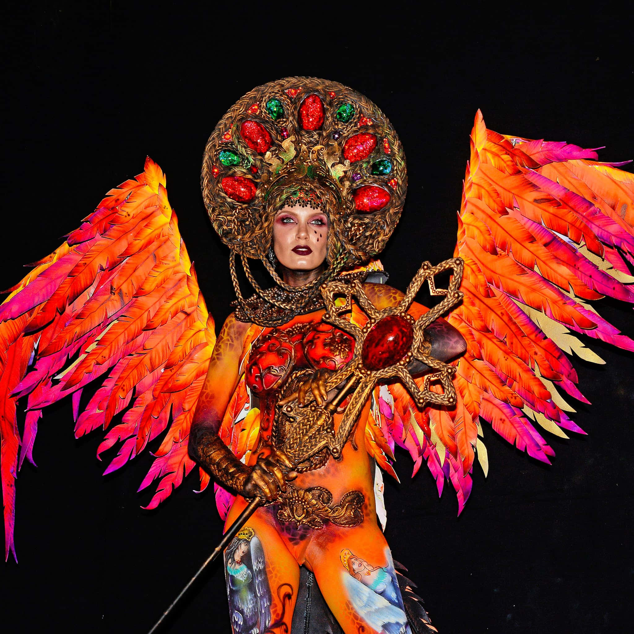 costume 桌布 壁紙 — 一個人穿著火熱的橙色和粉紅色羽毛天使服裝，戴著珠寶頭飾和華麗的身體彩繪，在黑色背景前擺姿勢。