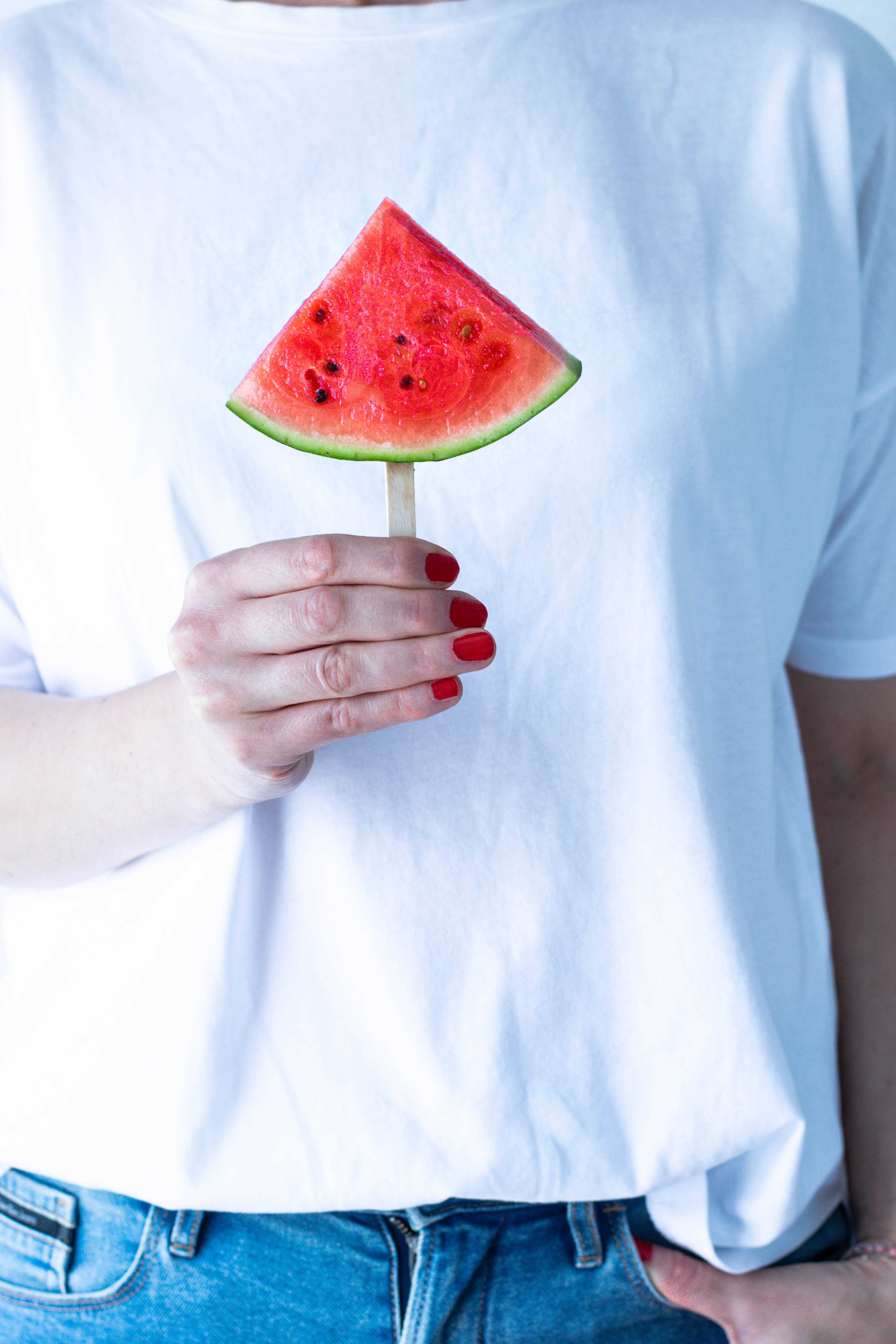 Watermelon 桌布 壁紙 — 一個人穿著白色T恤，在柔和日光下，用塗了紅色指甲油的手拿著一串鮮豔的西瓜片。