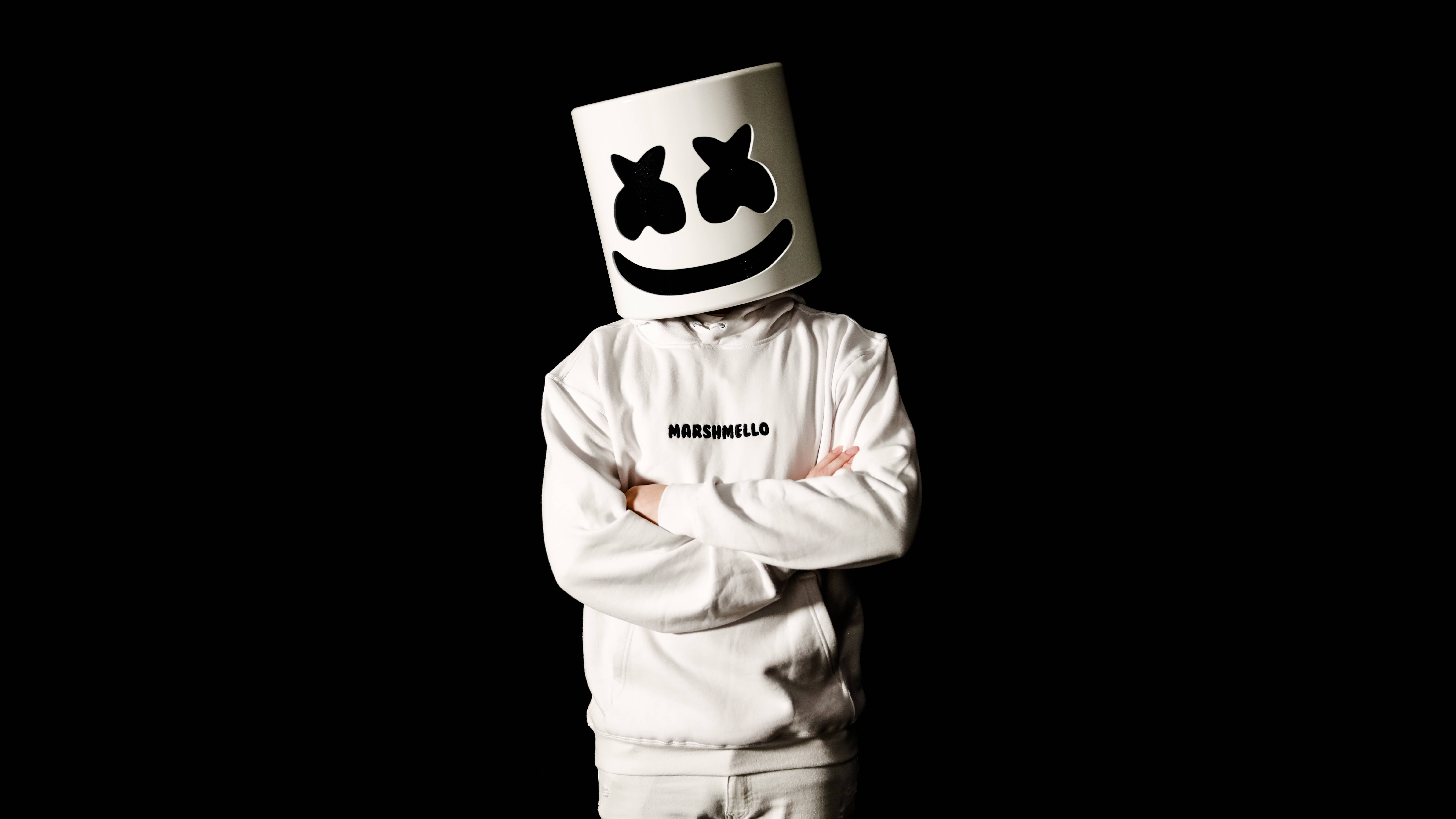 marshmello 4K 桌布 壁紙 — 一個人穿著白色連帽衫和標誌性的棉花糖頭盔，雙手交叉，站在黑色背景前。