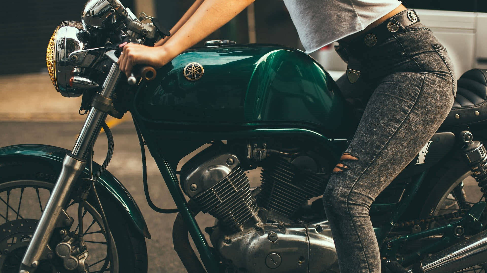 Bobber 桌布 壁紙 — 一個人穿著破洞牛仔褲跨坐在一輛光澤綠色復古機車上，帶有鍍鉻細節和黃色頭燈。