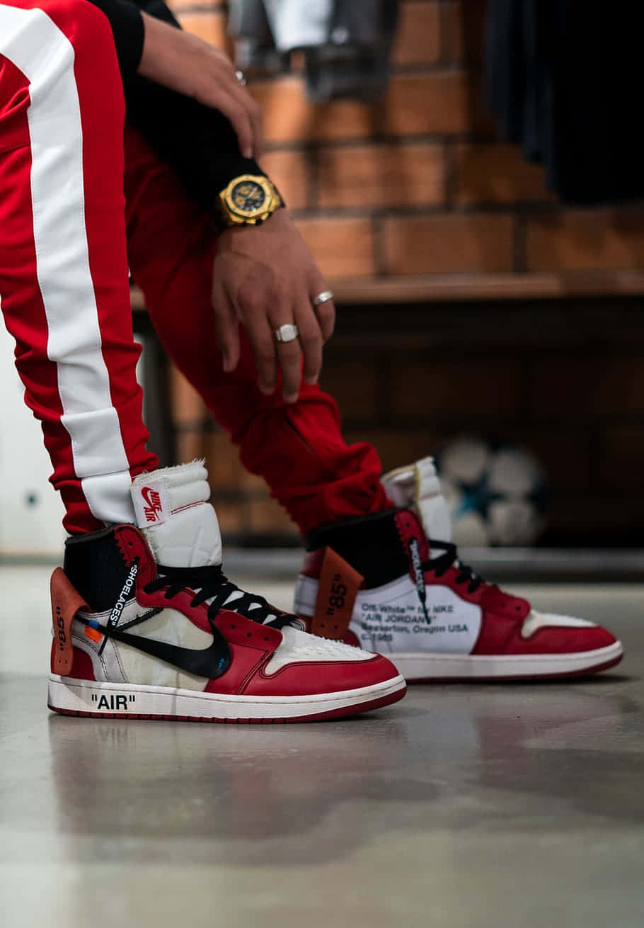 Jordan球鞋 桌布 壁紙 — 一個人穿著紅白色 Off-White x Nike Air Jordan 1 運動鞋，戴著金錶和戒指的特寫。