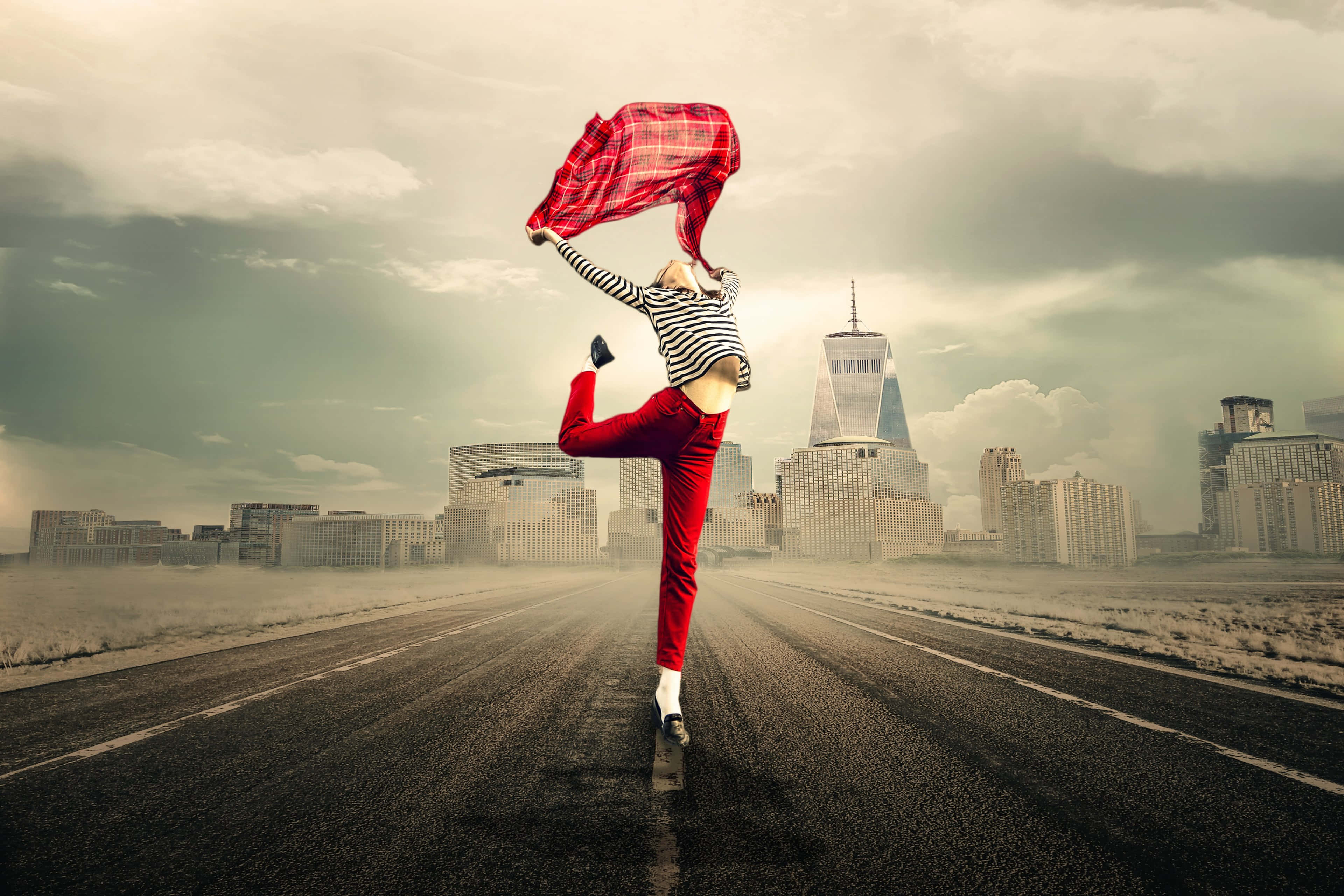 Freedom 桌布 壁紙 — 一個人穿著紅色褲子和條紋襯衫，在荒涼的高速公路上高高踢腿，一件紅色格紋襯衫在陰天城市天際線前飛揚。