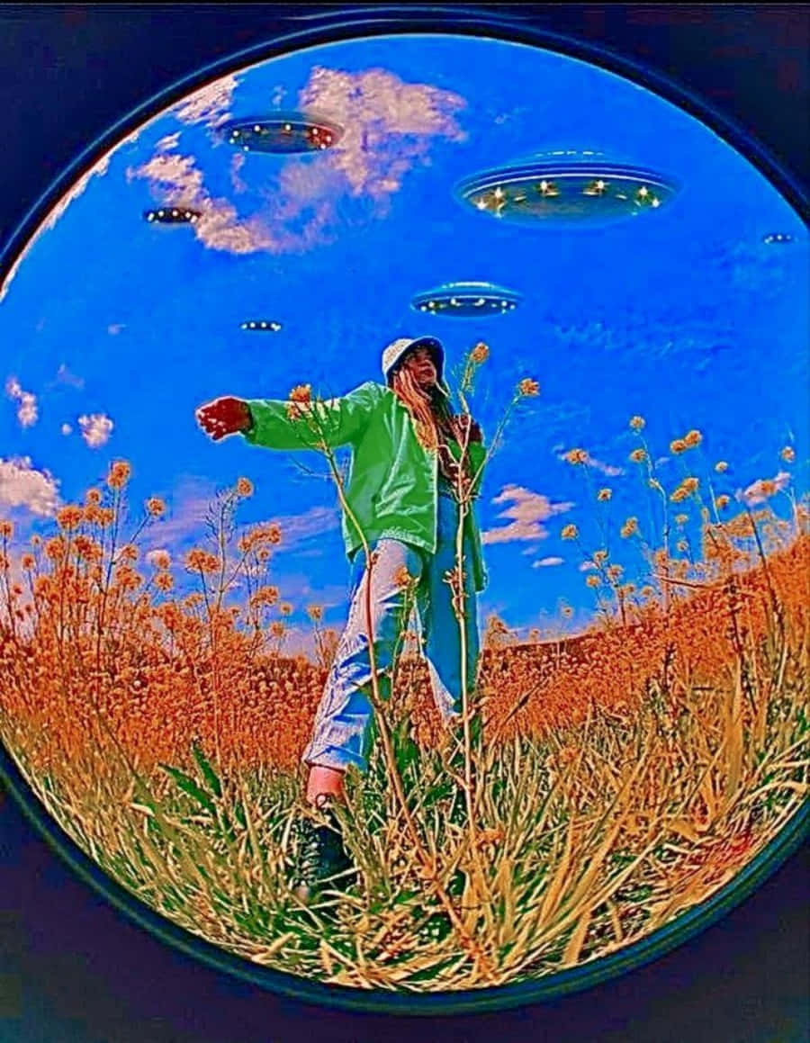 獨立 桌布 壁紙 — 一個人穿著綠色外套站在橙色花田裡，藍天佈滿UFO，透過魚眼鏡頭觀看。