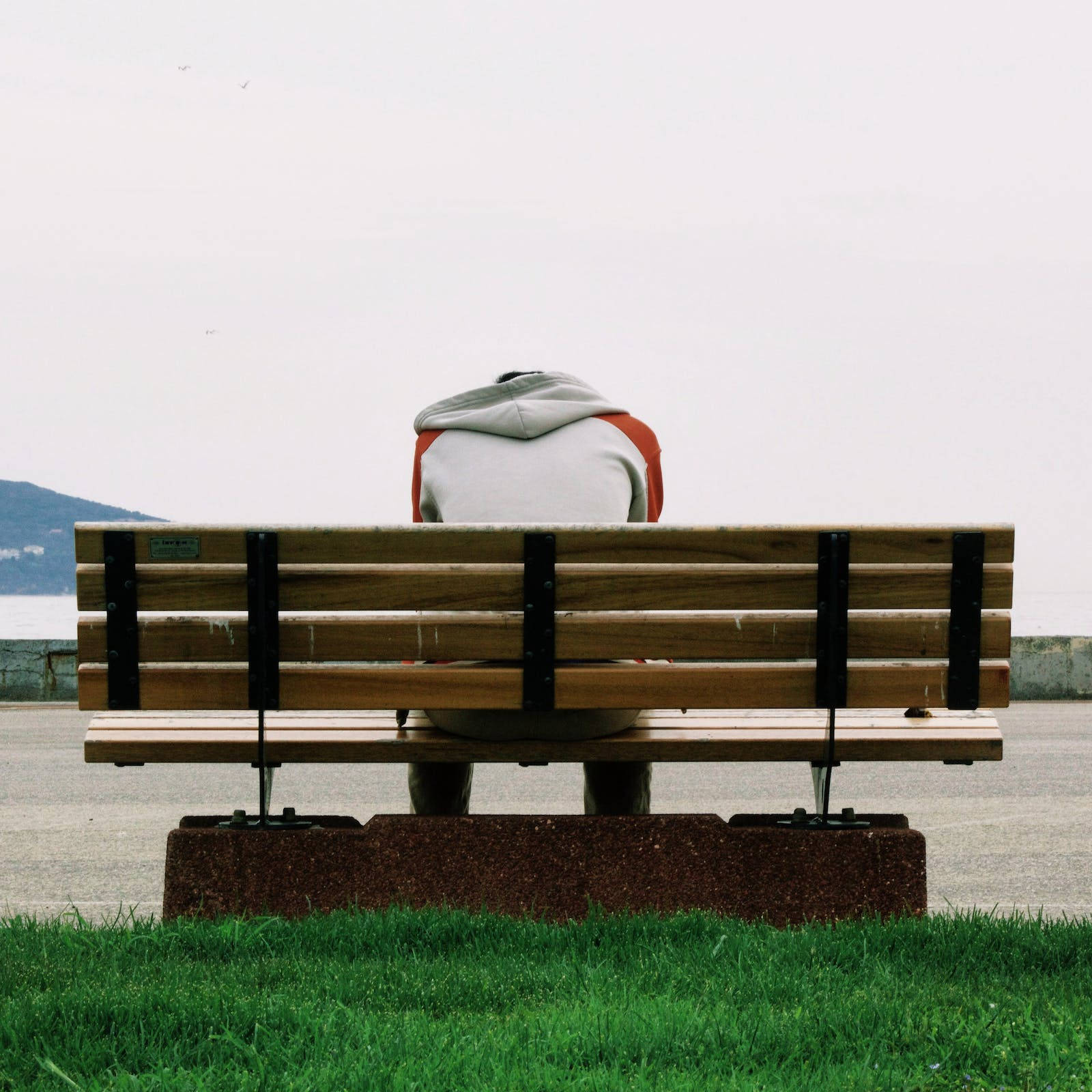 Lonely 桌布 壁紙 — 一個人穿著連帽上衣，獨自坐在木長椅上，俯瞰著陰天下一片平靜的大海。