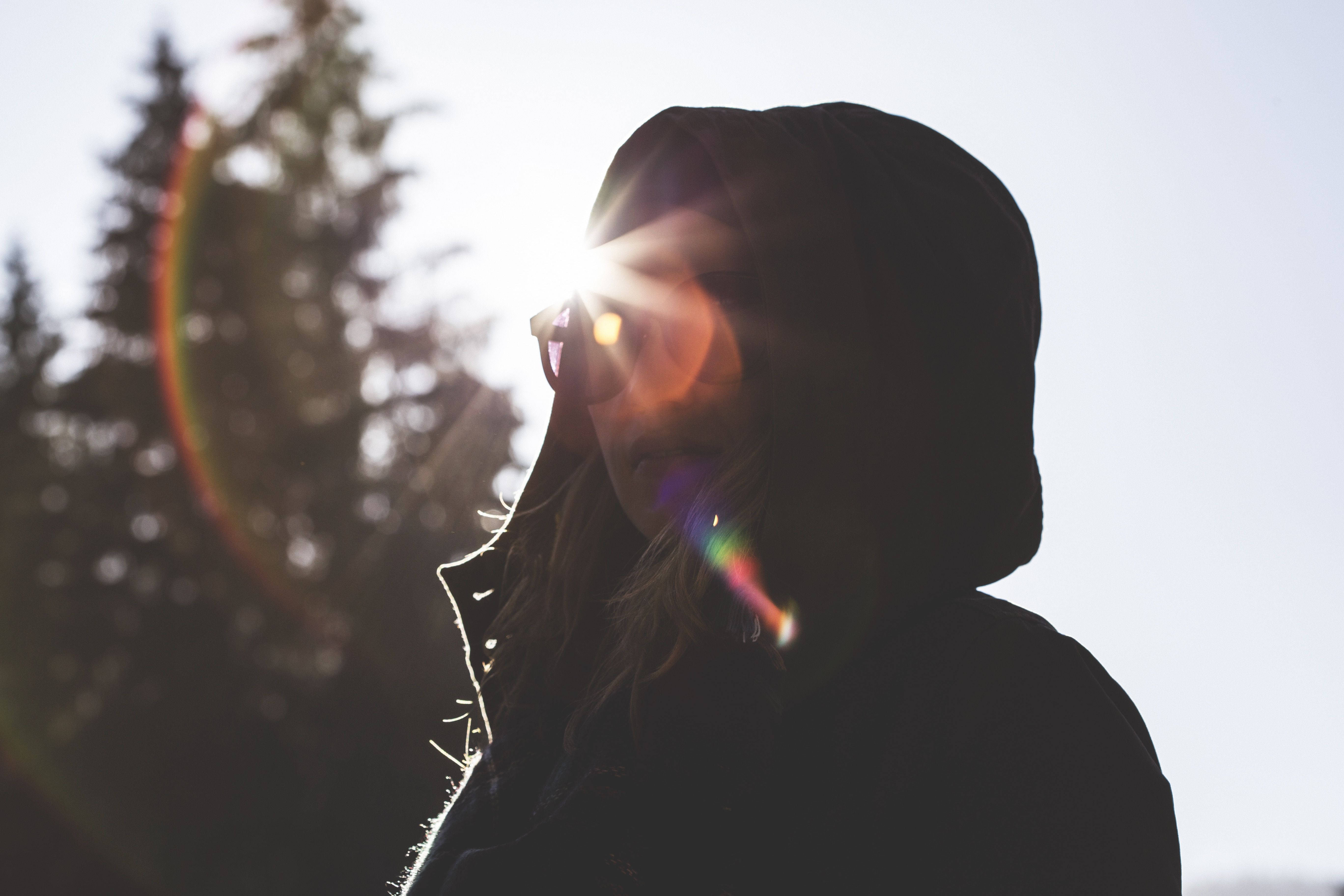 Sunshine 桌布 壁紙 — 一個人穿著連帽外套，在明亮的太陽、鏡頭光暈和松樹背景下形成剪影。