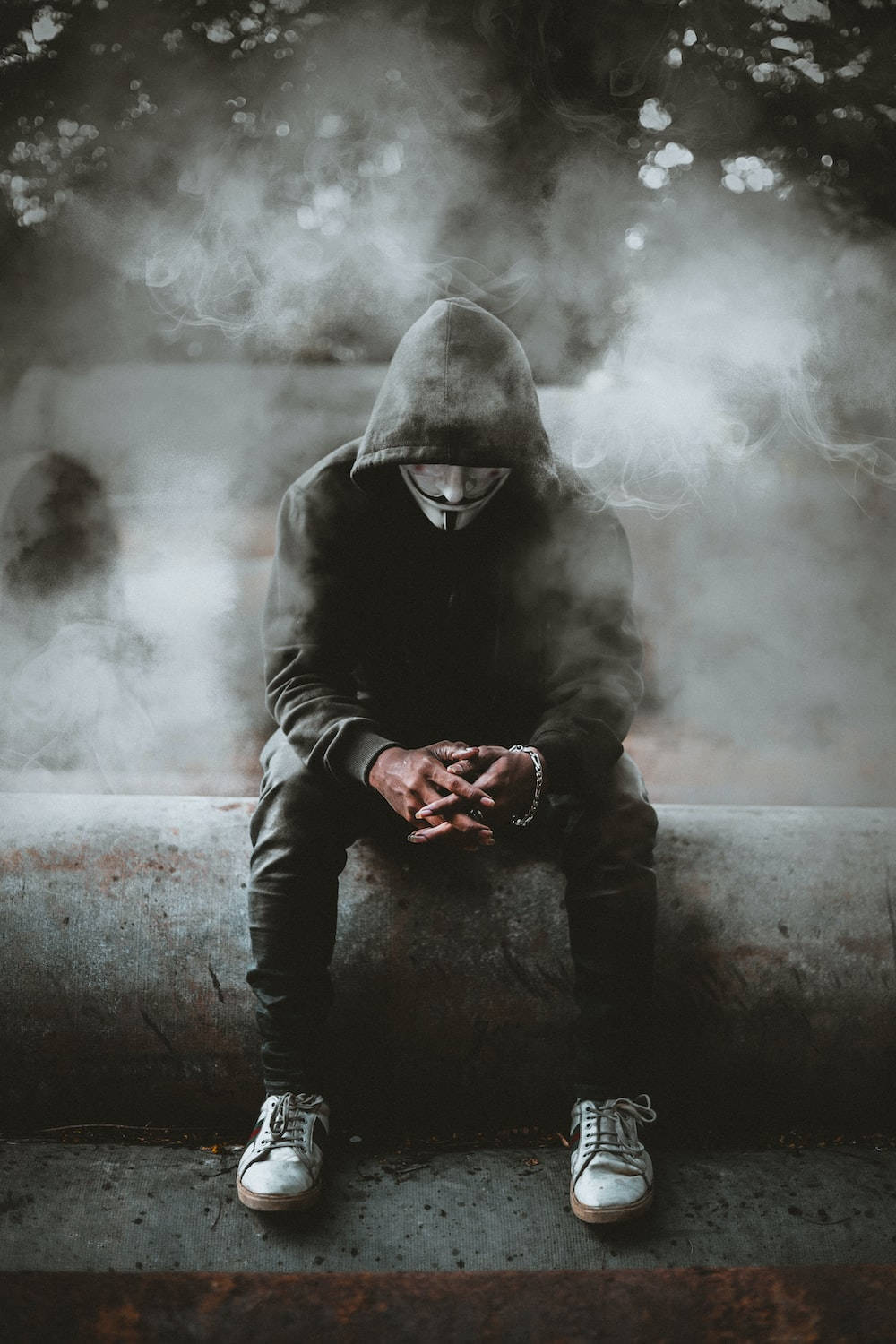 穿著連帽衫和面具的人坐在混凝土上，周圍有煙霧。 — 單身男孩 壁紙