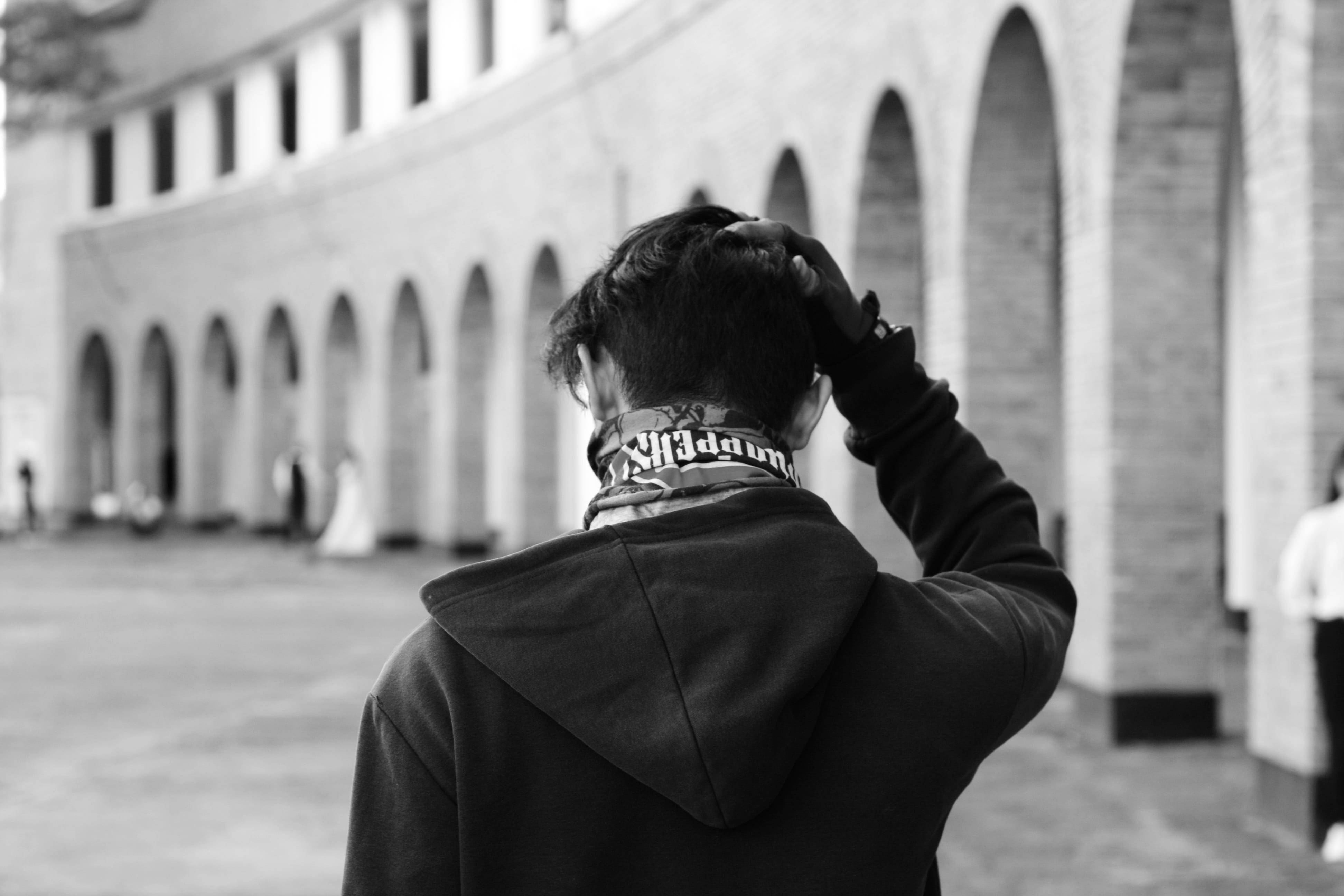 Alone Boy 桌布 壁紙 — 一個人穿著連帽衫背對鏡頭站立，手放在頭上，面前是一座長拱形磚建築，黑白風格。