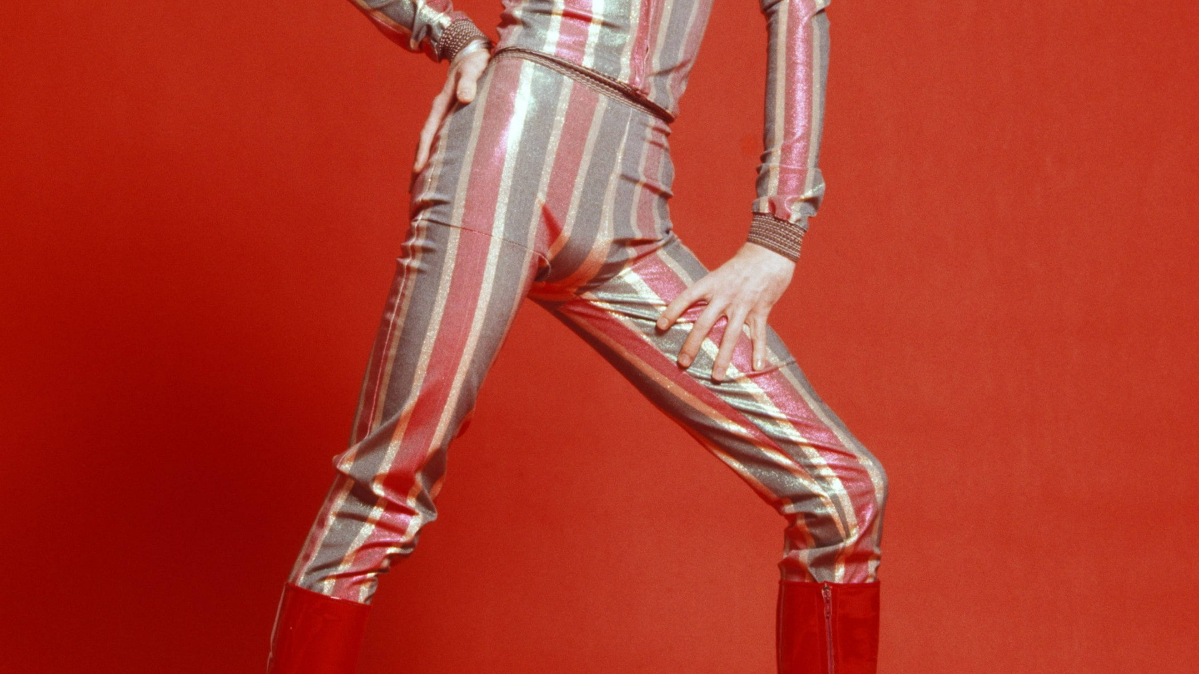 David Bowie 桌布 壁紙 — 一個人穿著閃亮條紋連身褲，在鮮紅色背景下擺出自信姿勢。