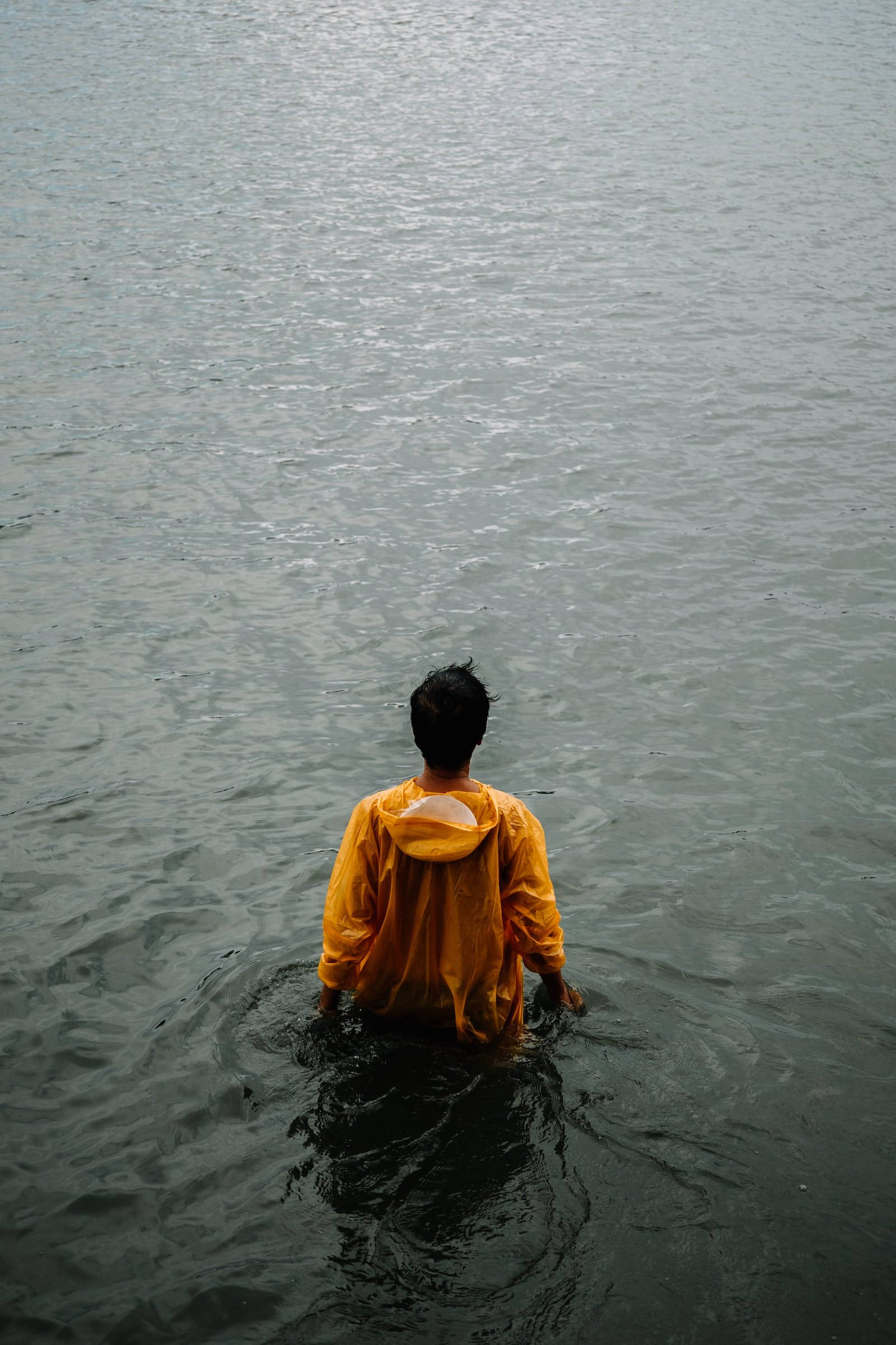 Lonely 桌布 壁紙 — 一個人穿著鮮黃色雨衣，腰部浸在平靜的灰色水中，從背後觀看。