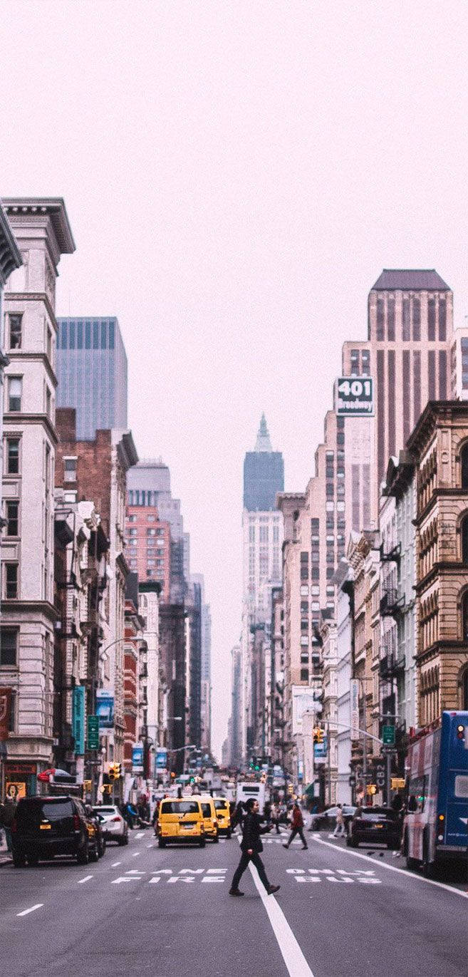 New York 桌布 壁紙 — 一個人穿過繁忙的城市街道，兩旁是高聳的建築物，天空朦朧，有黃色計程車和藍色巴士。