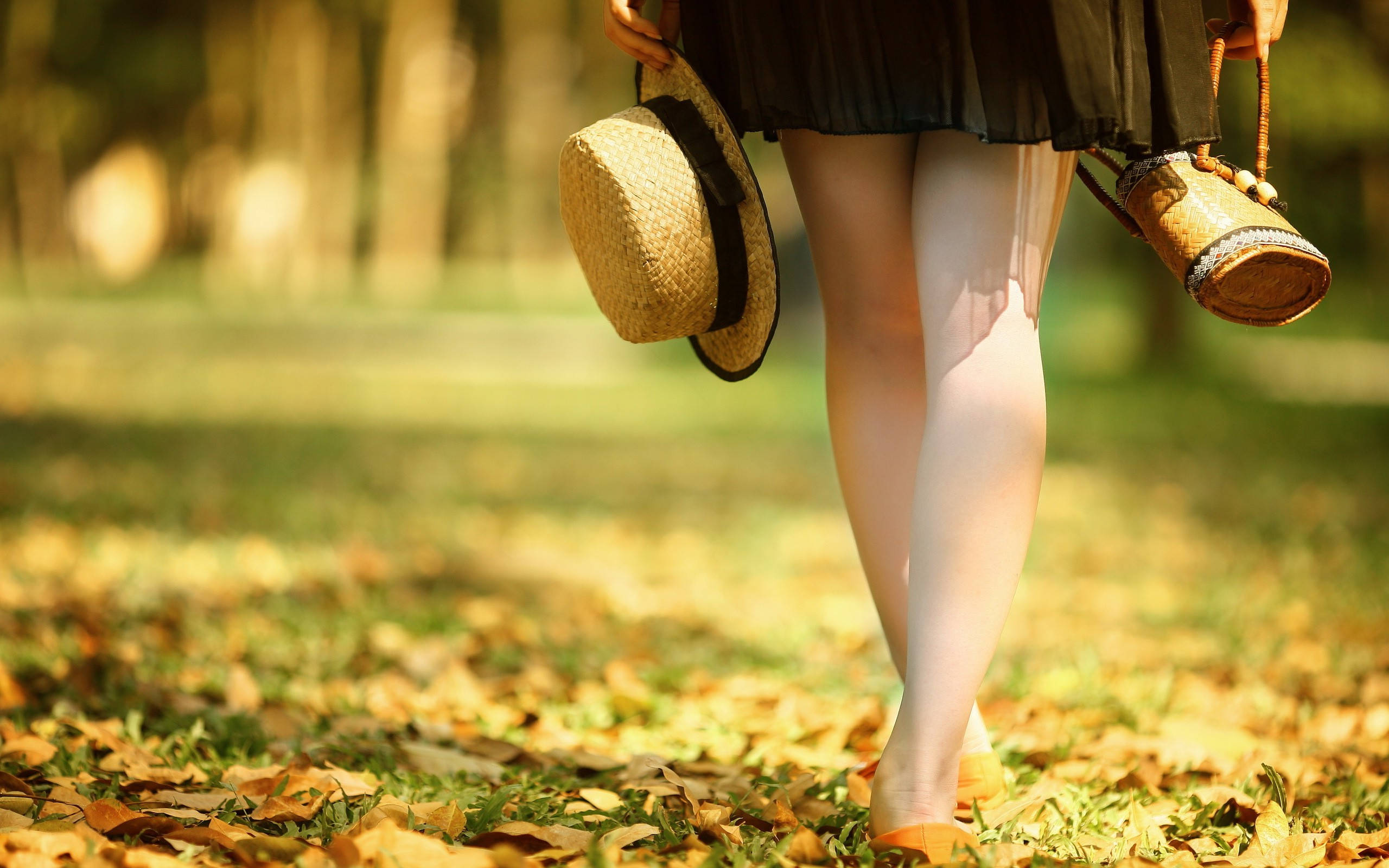 Woman 桌布 壁紙 — 一個人穿過陽光明媚的公園，穿著白色緊身褲，拿著草帽和編織袋，走在落葉地毯上。