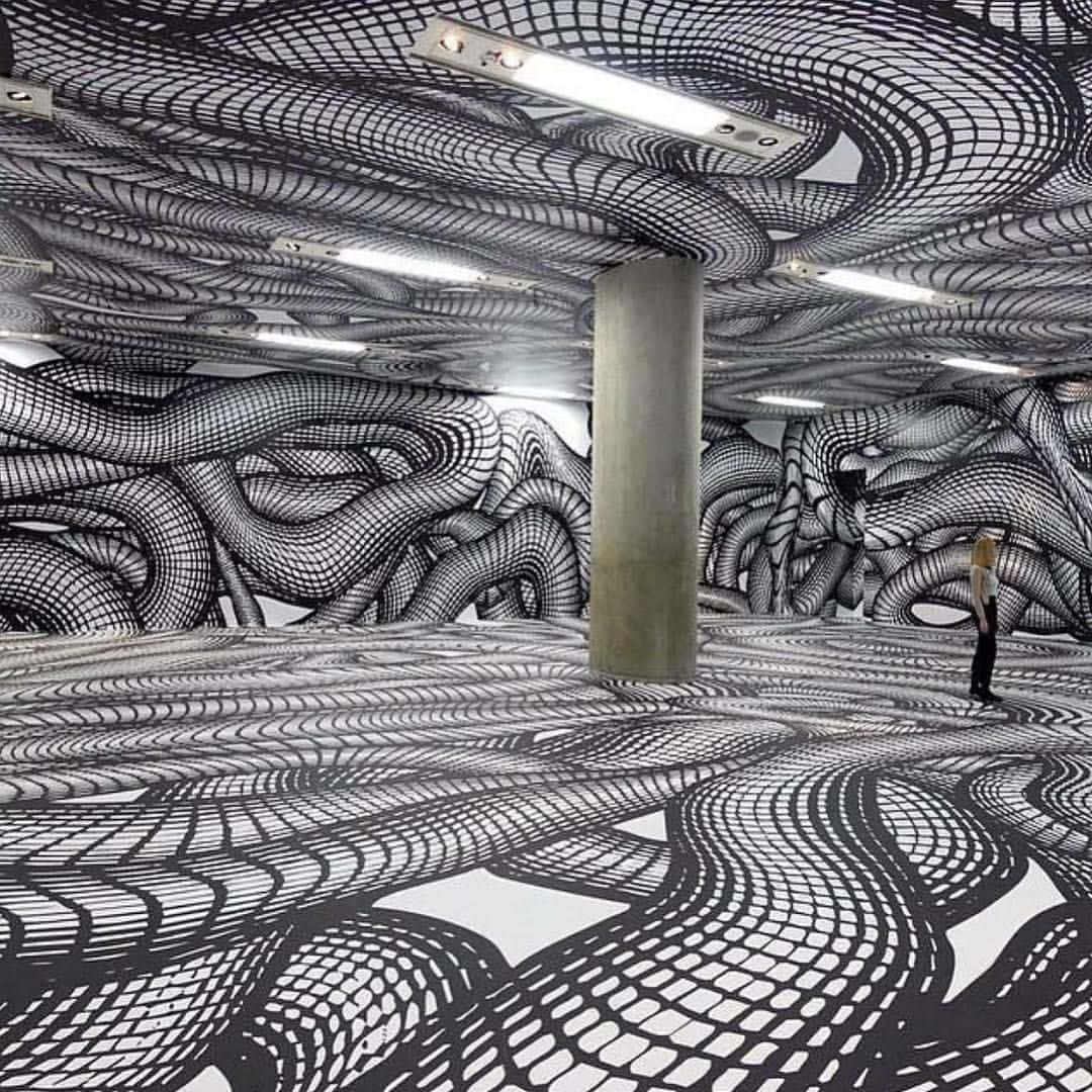 Installation Art 桌布 壁紙 — 一個人站在一個寬敞的房間裡，牆壁、天花板和地板在螢光燈下覆蓋著旋轉的黑白錯視圖案。