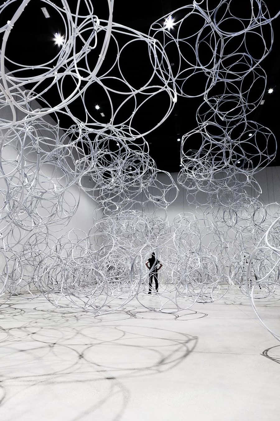 Installation Art 桌布 壁紙 — 一個人站在一個寬敞的白色畫廊中，被懸掛的發光白色圓形管道的沉浸式裝置襯托得渺小。