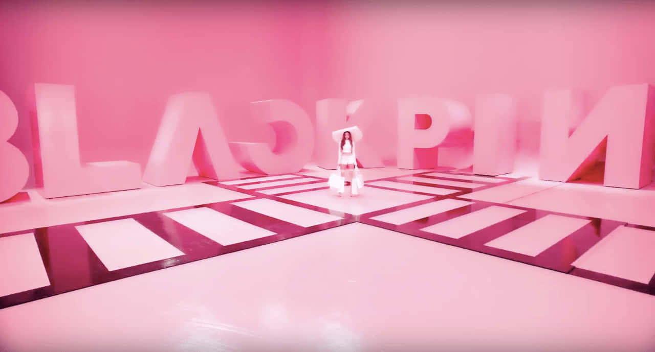 桌布 壁紙 — 一個人站在單色粉紅色房間的中央舞台，有巨大的「BLACKPINK」字母和反射的棋盤地板。