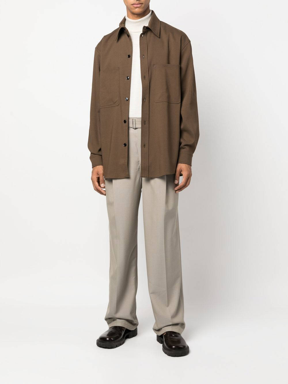 Mens Fashion 桌布 壁紙 — 一個人站在攝影棚，穿著一件棕色鈕扣襯衫，內搭白色高領衫，搭配米色褲子和黑色鞋子。
