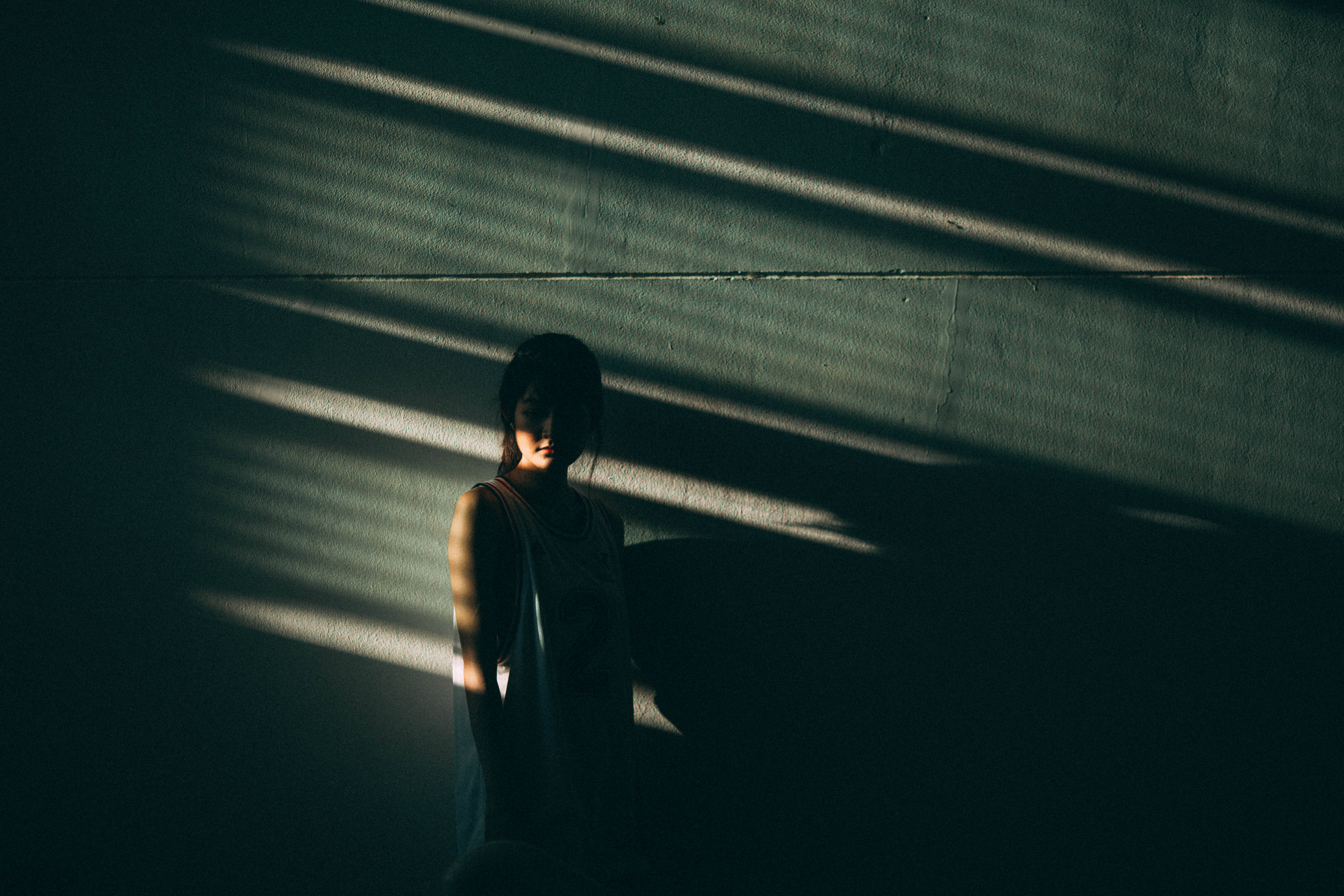 Sad Alone 桌布 壁紙 — 一個人站在昏暗的房間裡，戲劇性的條紋陽光在紋理牆壁上投下長長的陰影。