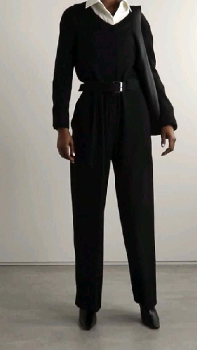Black Clothing 桌布 壁紙 — 一個人站在極簡風格的工作室空間，穿著黑色寬腿連身褲、白色有領襯衫和黑色腰帶。