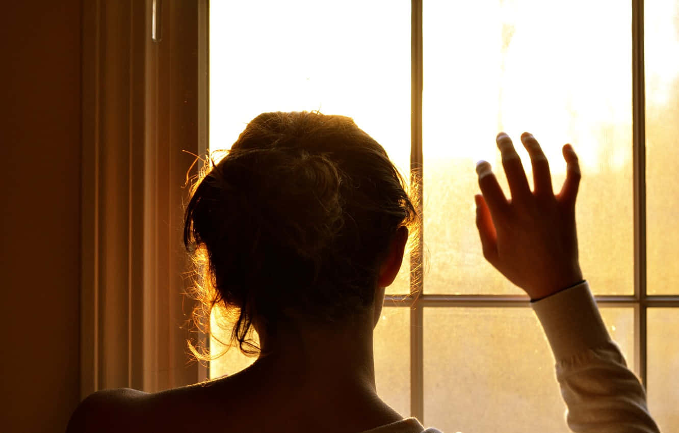 Woman Silhouette 桌布 壁紙 — 一個人站在陽光照射的窗邊，伸出一隻手，金色的光線穿過玻璃。