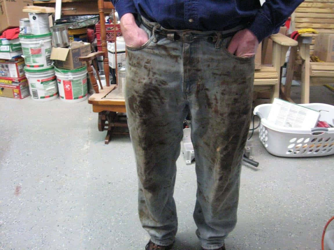 Dirty 桌布 壁紙 — 一個人站在雜亂的工場，穿著嚴重污漬的工作褲，雙手插在口袋裡。