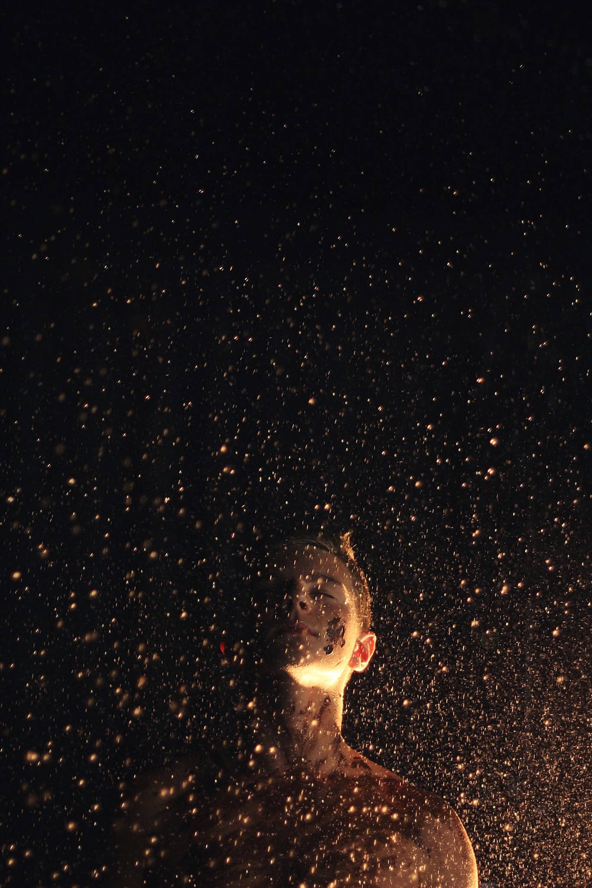 Dust 桌布 壁紙 — 一個人站在黑色背景前，沐浴在金色火花的暖光下。