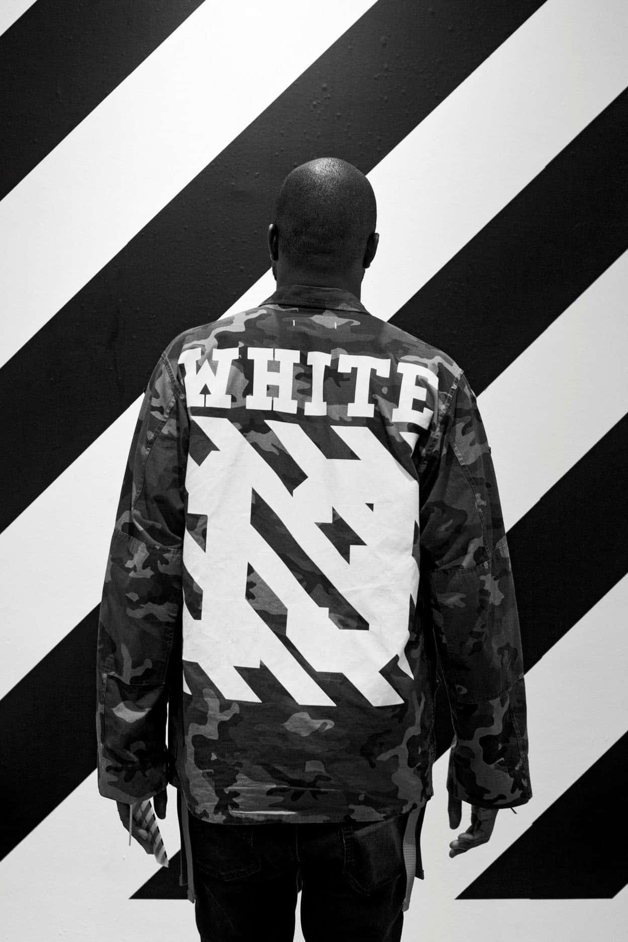 Off White iPhone 桌布 壁紙 — 一個人背對鏡頭站立，身穿迷彩外套，上面有粗體白色「WHITE」文字和圖案，背景是黑白對角條紋牆。