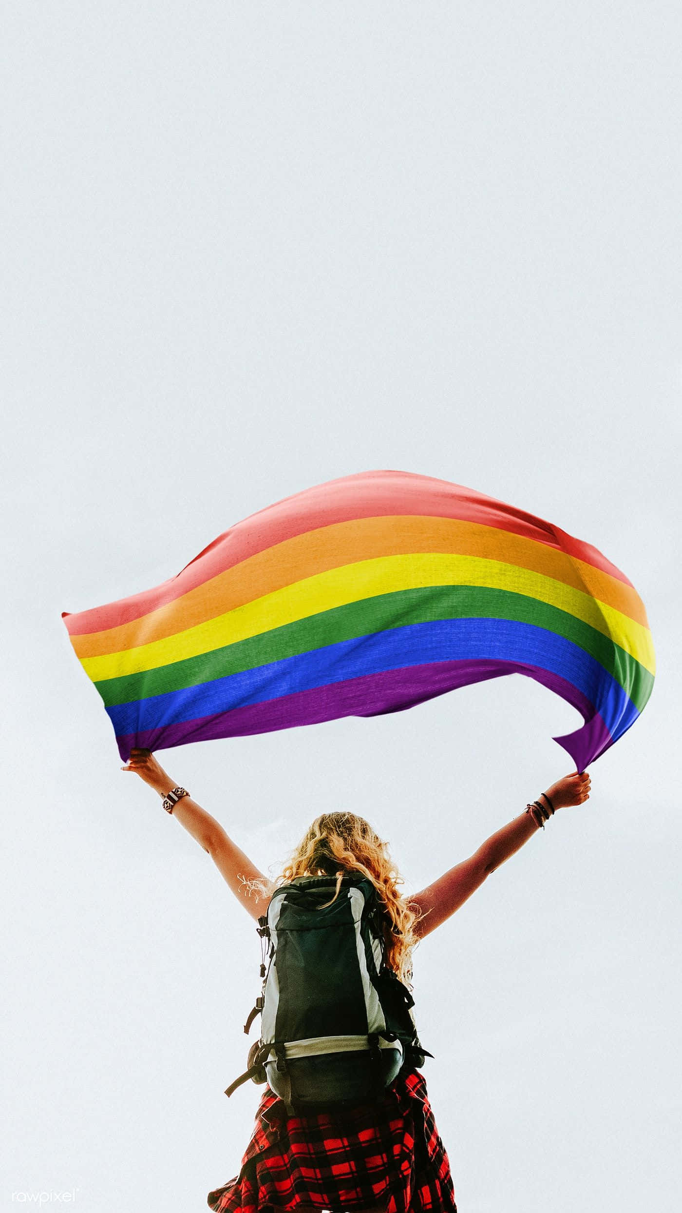 LGBT 桌布 壁紙 — 一個人背著背包，在蒼白的天空高舉鮮豔的彩虹旗。