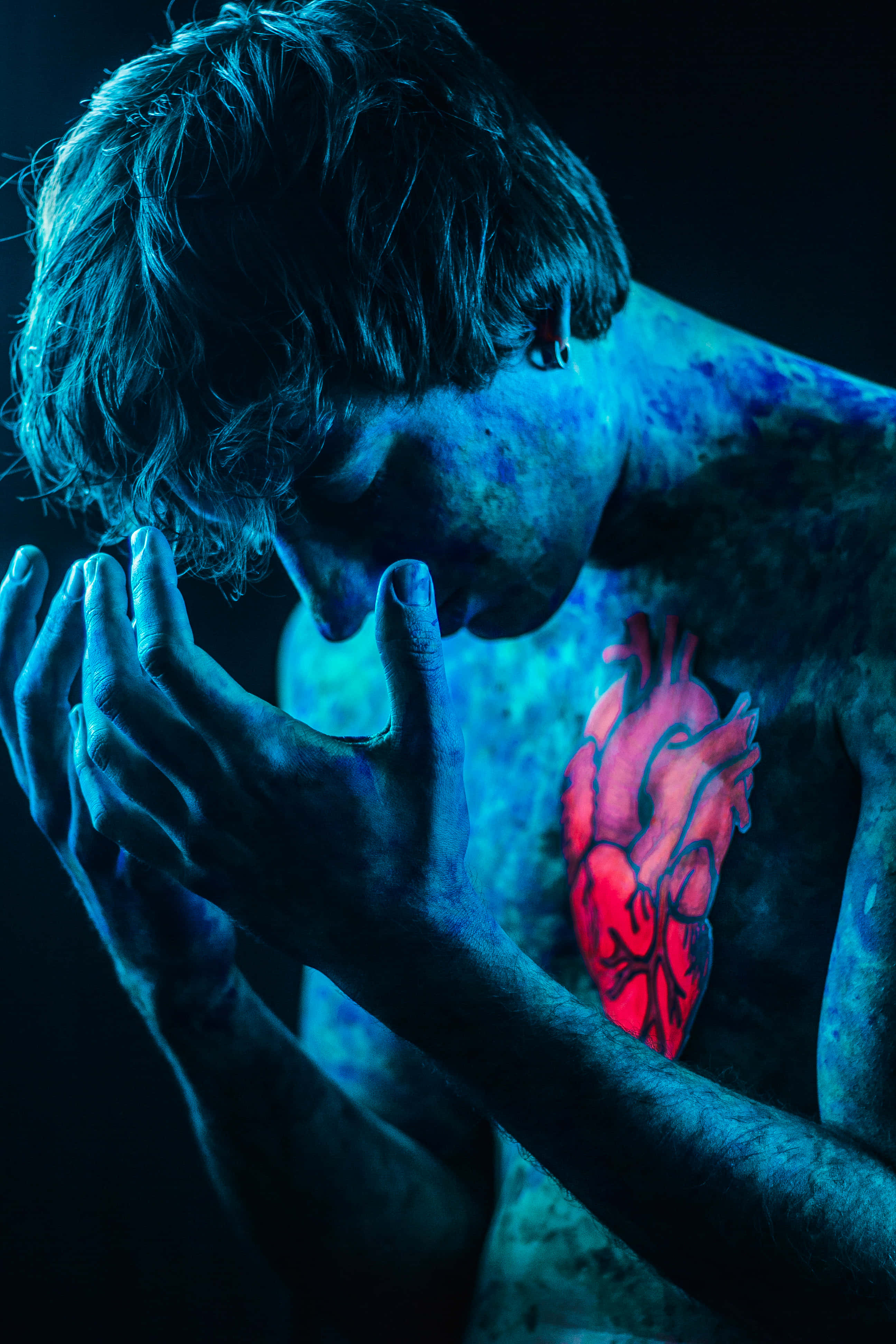 Dark Emotional 桌布 壁紙 — 一個人胸前有一個發光的紅色解剖心形紋身，在藍色燈光照射下，雙手合十，處於情感強烈的時刻。