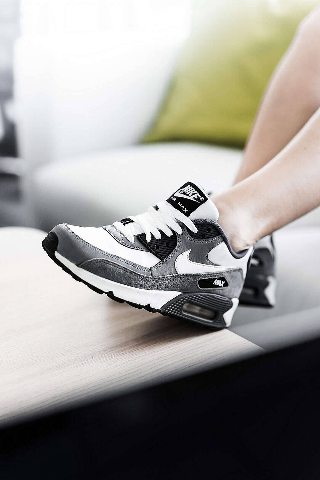 一個人腳部穿著灰色和白色的Nike Air Max運動鞋在木質表面上。