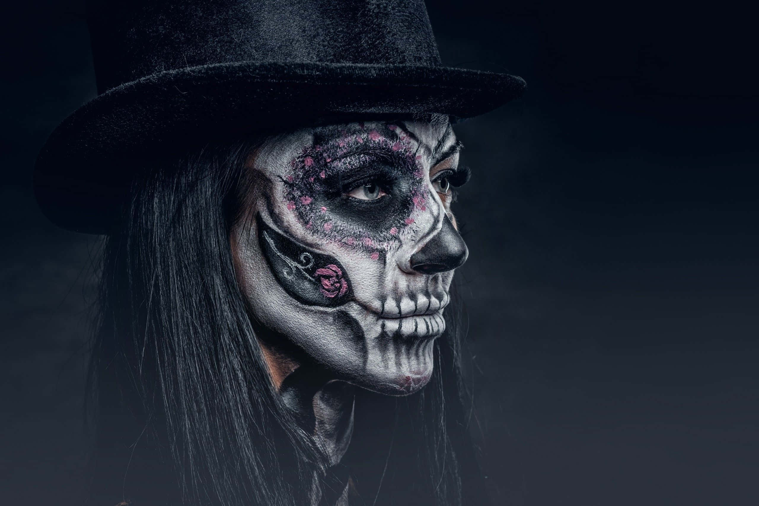 Day Of The Dead 桌布 壁紙 — 一個人臉上畫著精緻的糖骷髏妝，戴著黑色高頂帽，在陰暗憂鬱的背景前莊嚴地凝視。