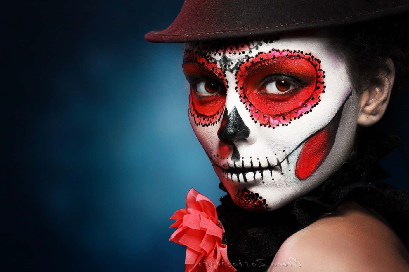Halloween Face Paint 桌布 壁紙 — 一個人臉上畫著精緻的糖骷髏妝容，手持紅玫瑰，背景為深藍色。