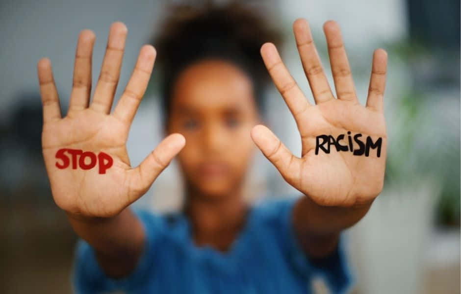 stop 桌布 壁紙 — 一個人舉起雙手，手掌上寫有紅色的「STOP」和黑色的「RACISM」，背景中模糊的臉。