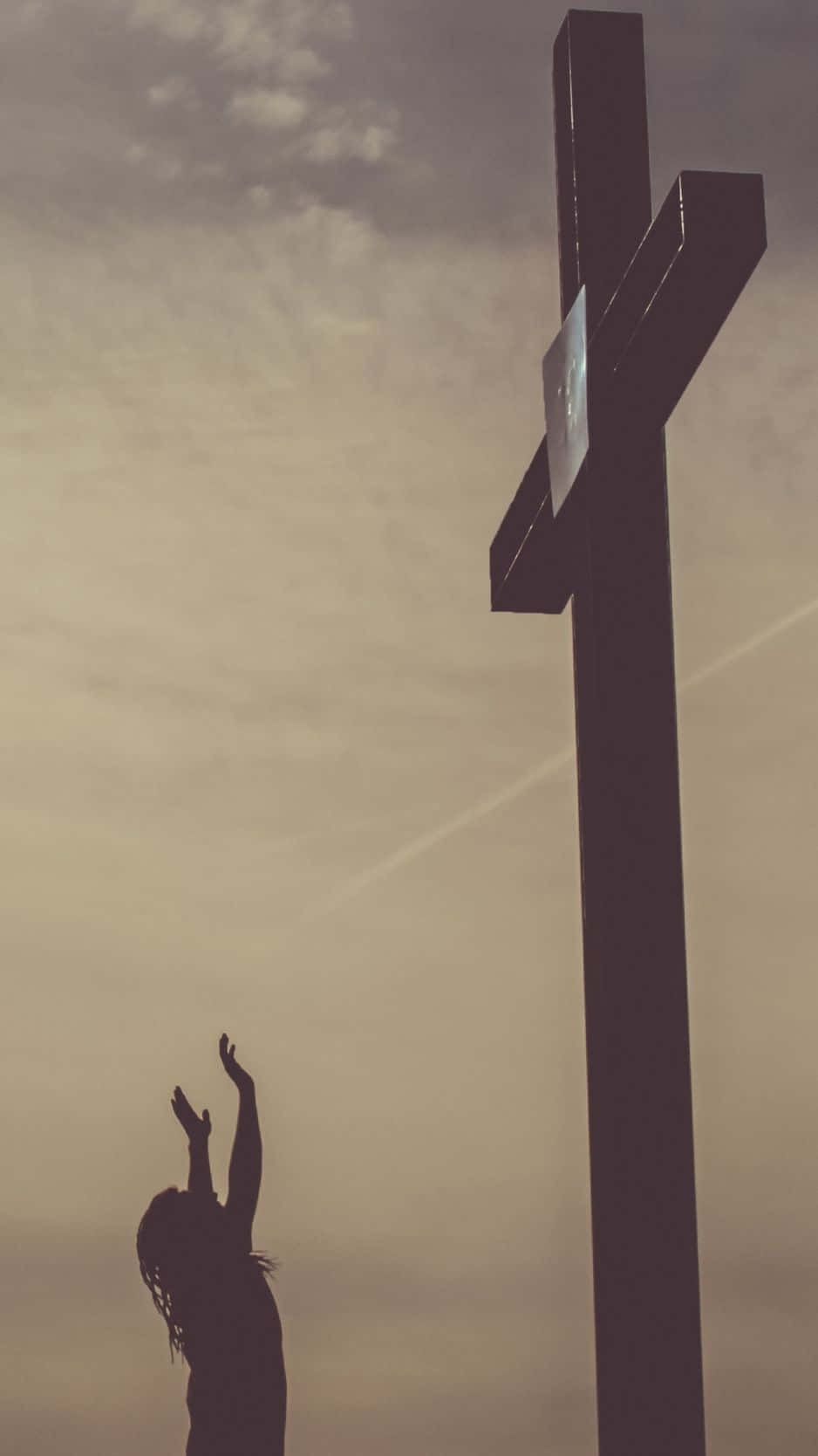 Cross iPhone 桌布 壁紙 — 一個人舉起雙臂祈禱的剪影，背景是陰雲密布的天空中高聳的十字架。