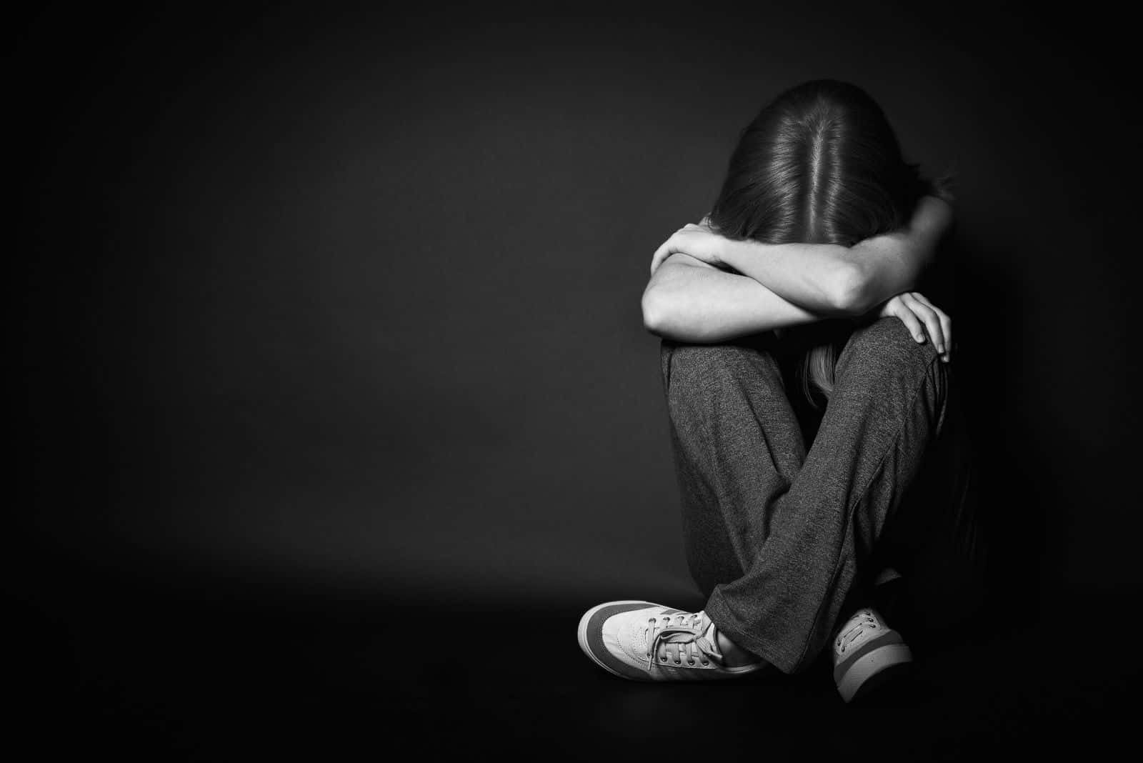 Depressed 桌布 壁紙 — 一個人蜷縮坐在黑暗工作室的地板上，雙臂環抱膝蓋，頭埋在寂靜中。