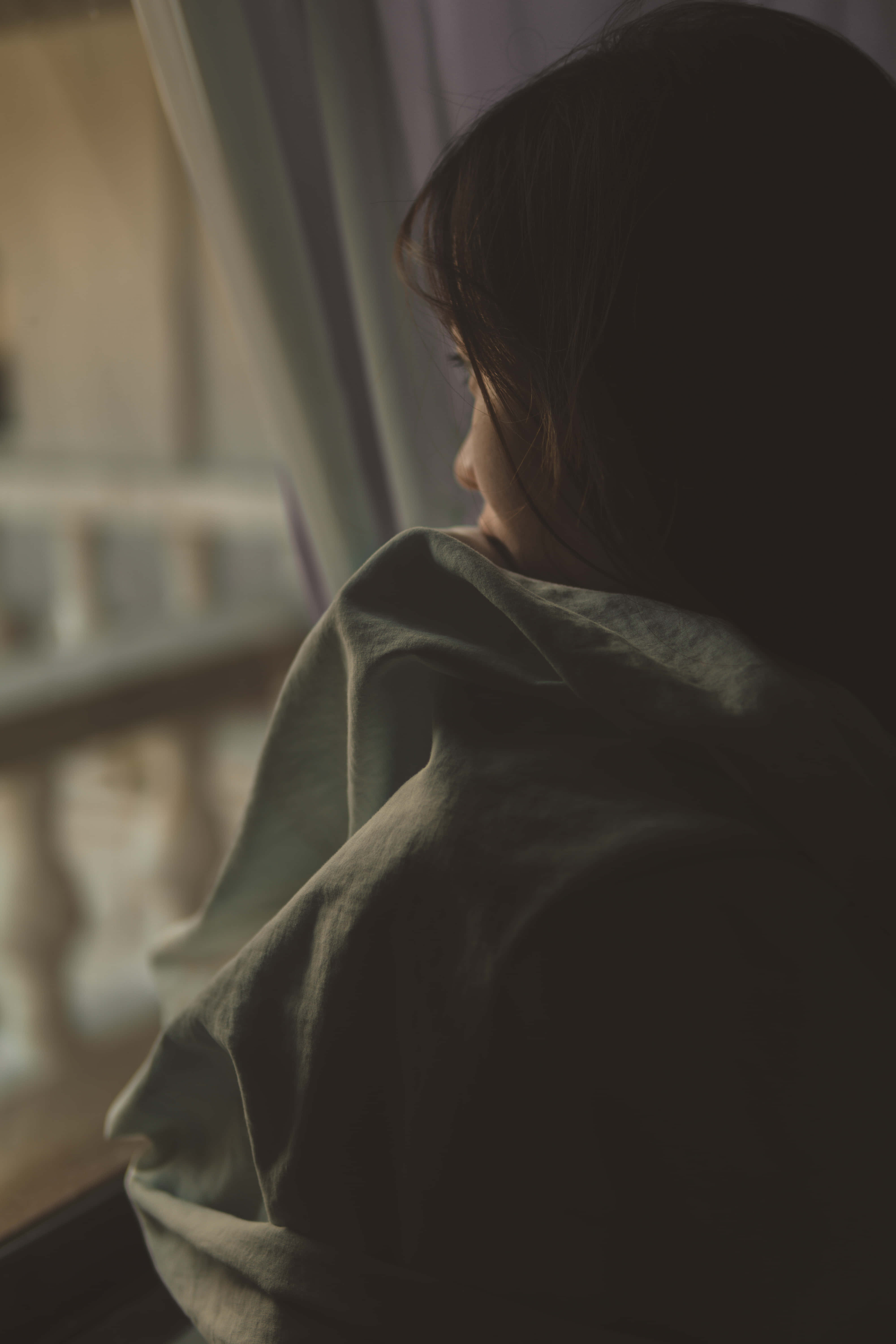 Depression Girl 桌布 壁紙 — 一個人裹著柔軟的毯子，若有所思地望著窗外，窗外沐浴在溫暖的金色光芒中。