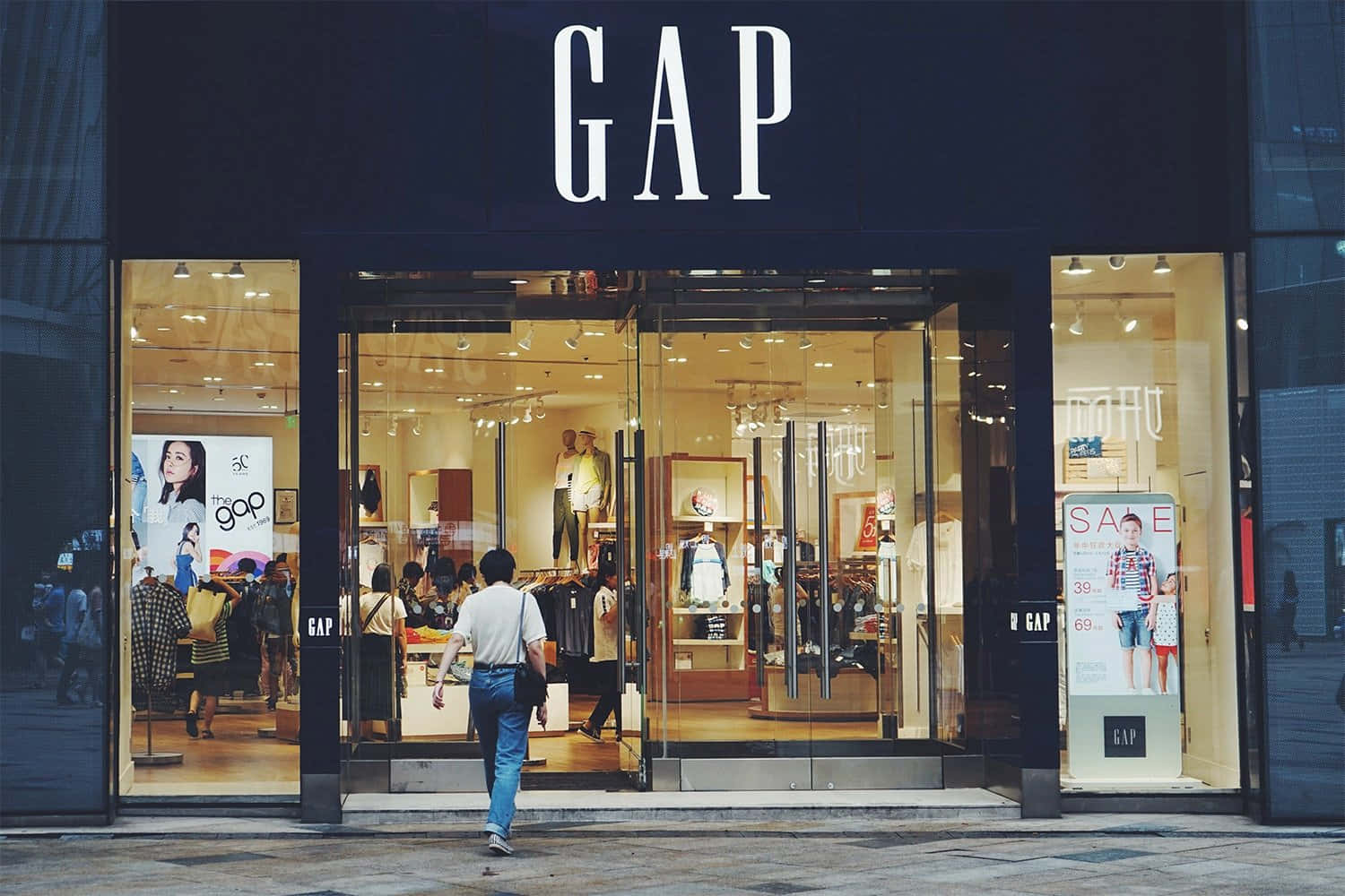 間隙 桌布 壁紙 — 一個人走過一間燈光明亮的GAP服裝店，店內有玻璃門和模特兒。