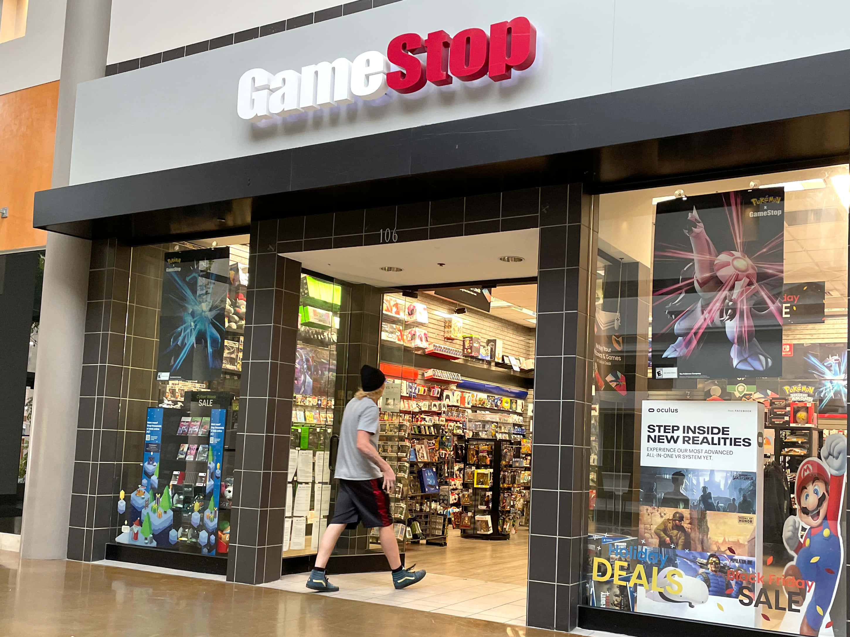 Gamestop 桌布 壁紙 — 一個人走過商場內燈光明亮的GameStop店鋪，展示著電子遊戲海報和商品。