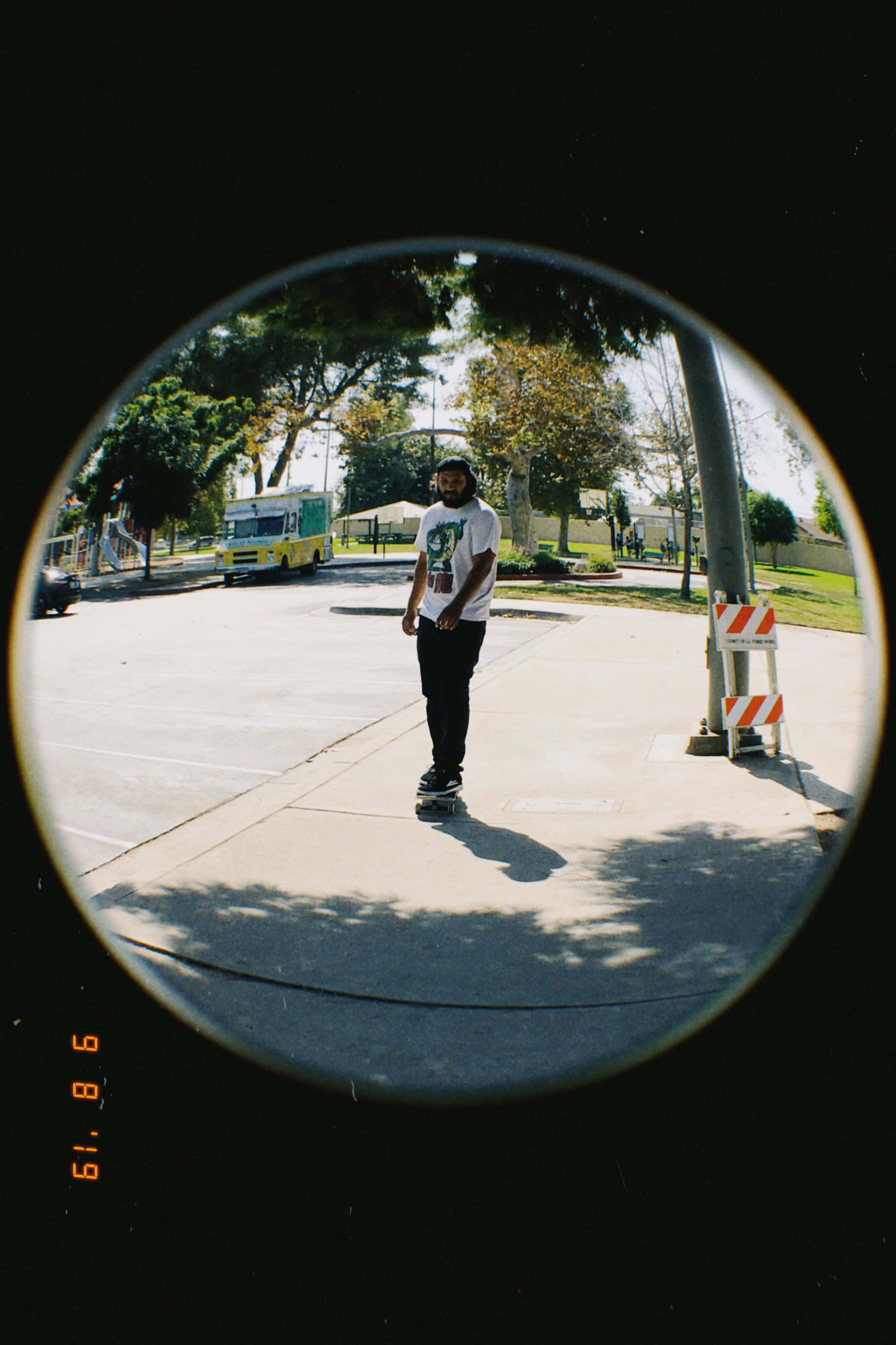 Fisheye 桌布 壁紙 — 一個人踩著滑板穿過一個圓形魚眼鏡頭視角，背景是陽光明媚的城市街道，有樹木和美食車。